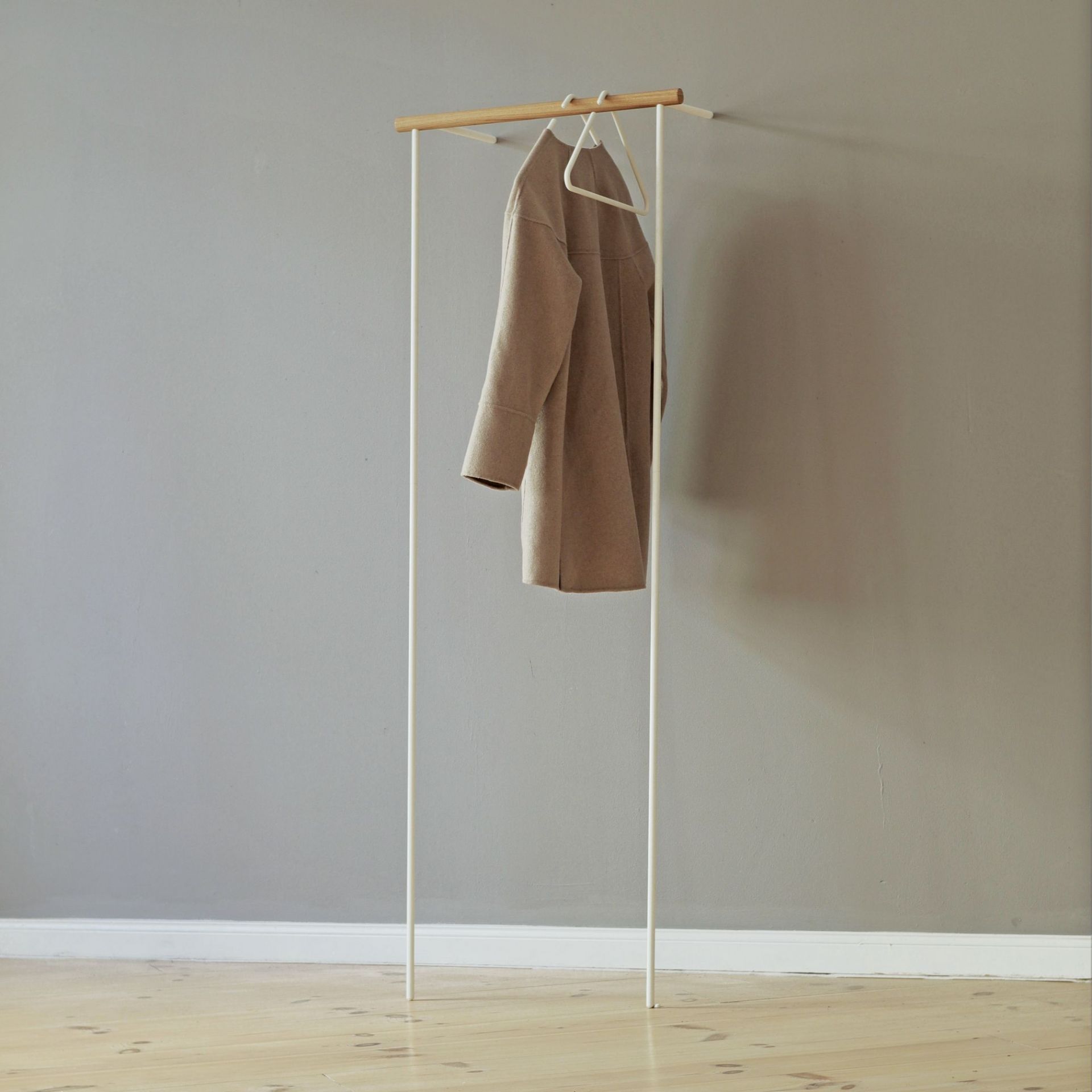 Weiße Leanon II Anlehngarderobe von Roomsafari mit Mantel an der Wand. Moderne Garderobenlösung.