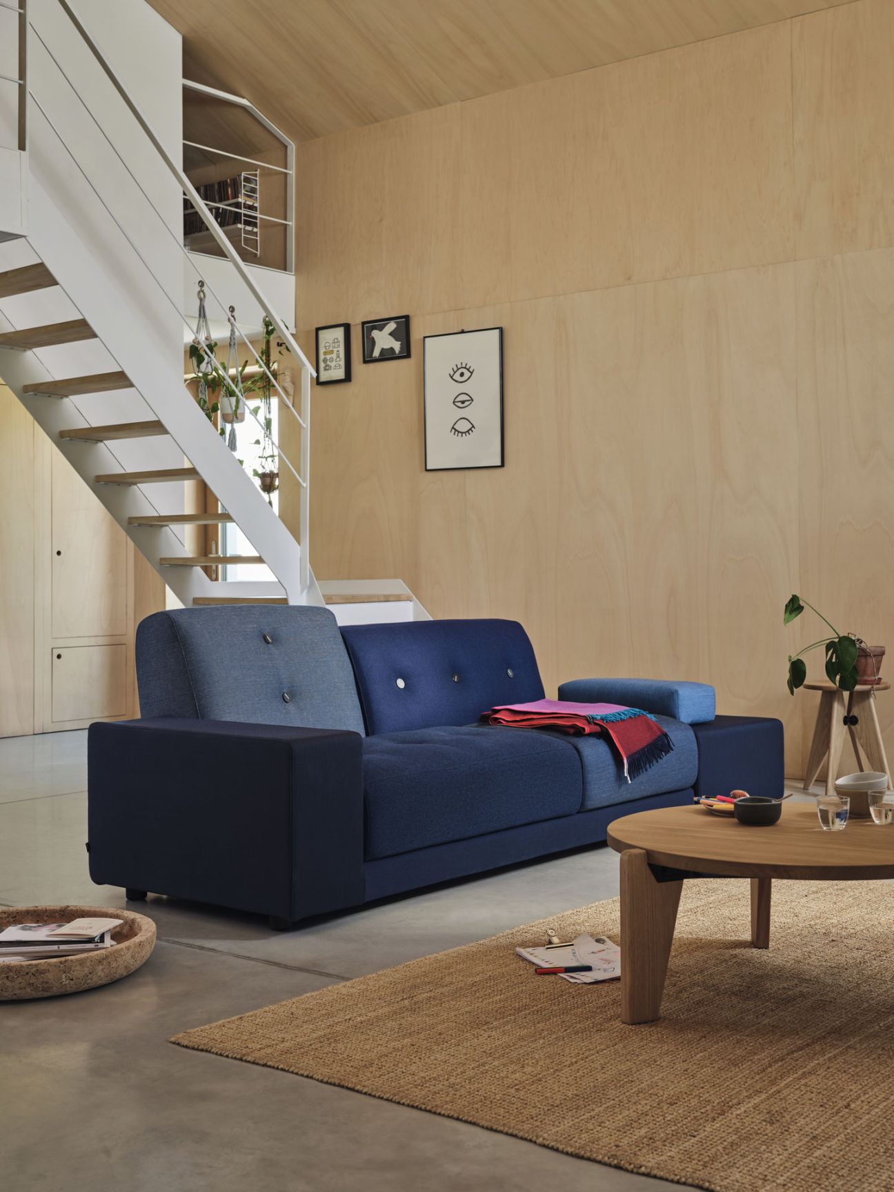 Blaues Polder Sofa von Vitra in modernem Wohnzimmer mit Holzwand und Teppich.