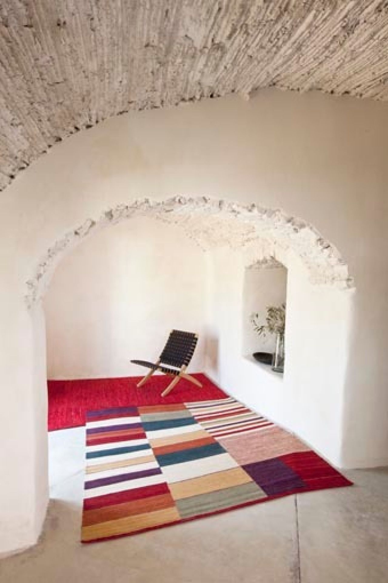 Medina Teppich von Nanimarquina, 200x300 cm, mit bunten Streifen in einem Raum mit Gewölbe.