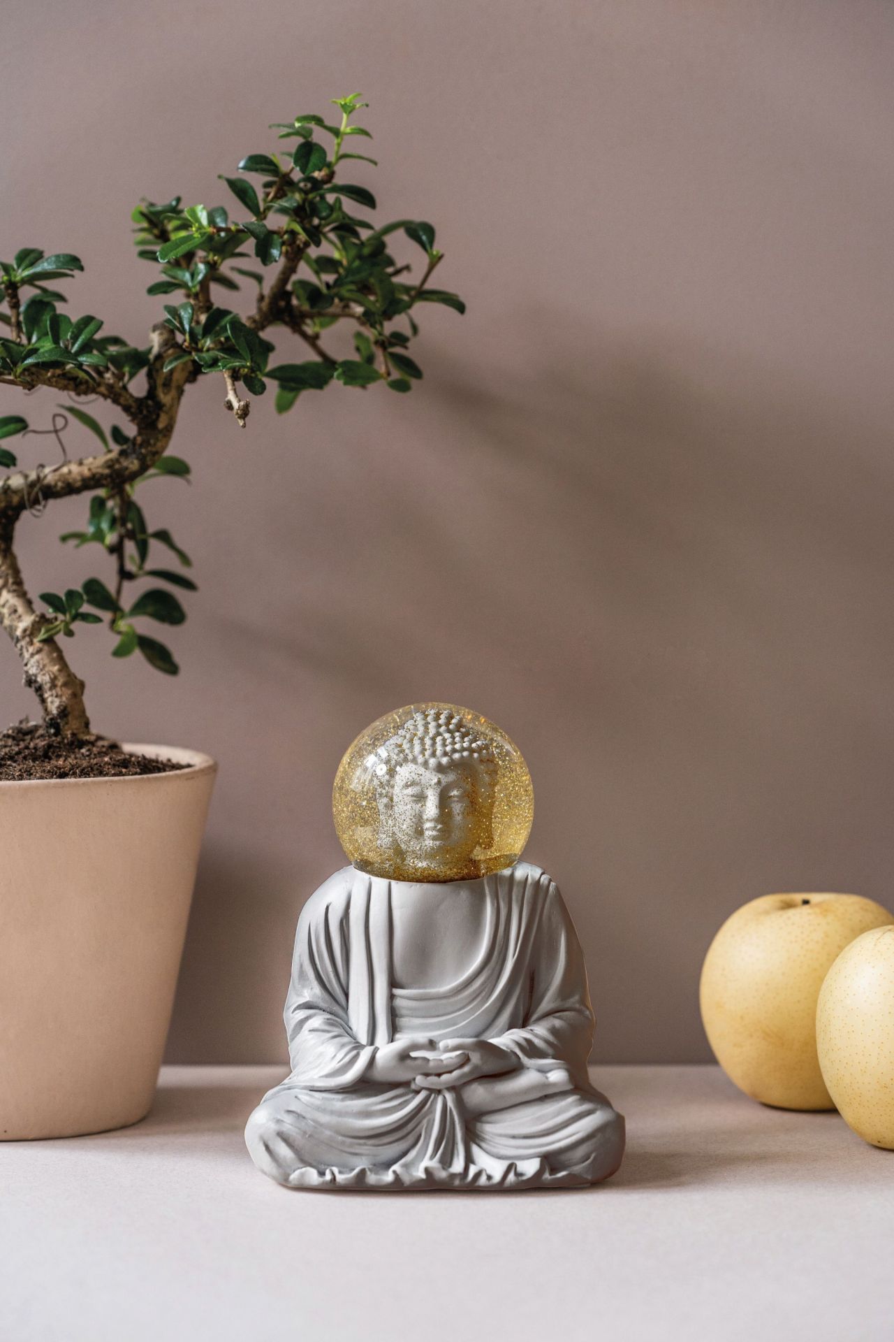 Graue Buddha Figur mit Glitzerkugel als Kopf, neben Bonsai und Birnen. Summerglobes Dekoration.