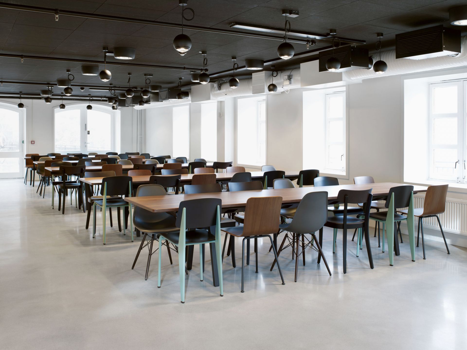 Innenaufnahme: Viele Vitra Hal Ply Stühle in verschiedenen Farben an Holztischen.