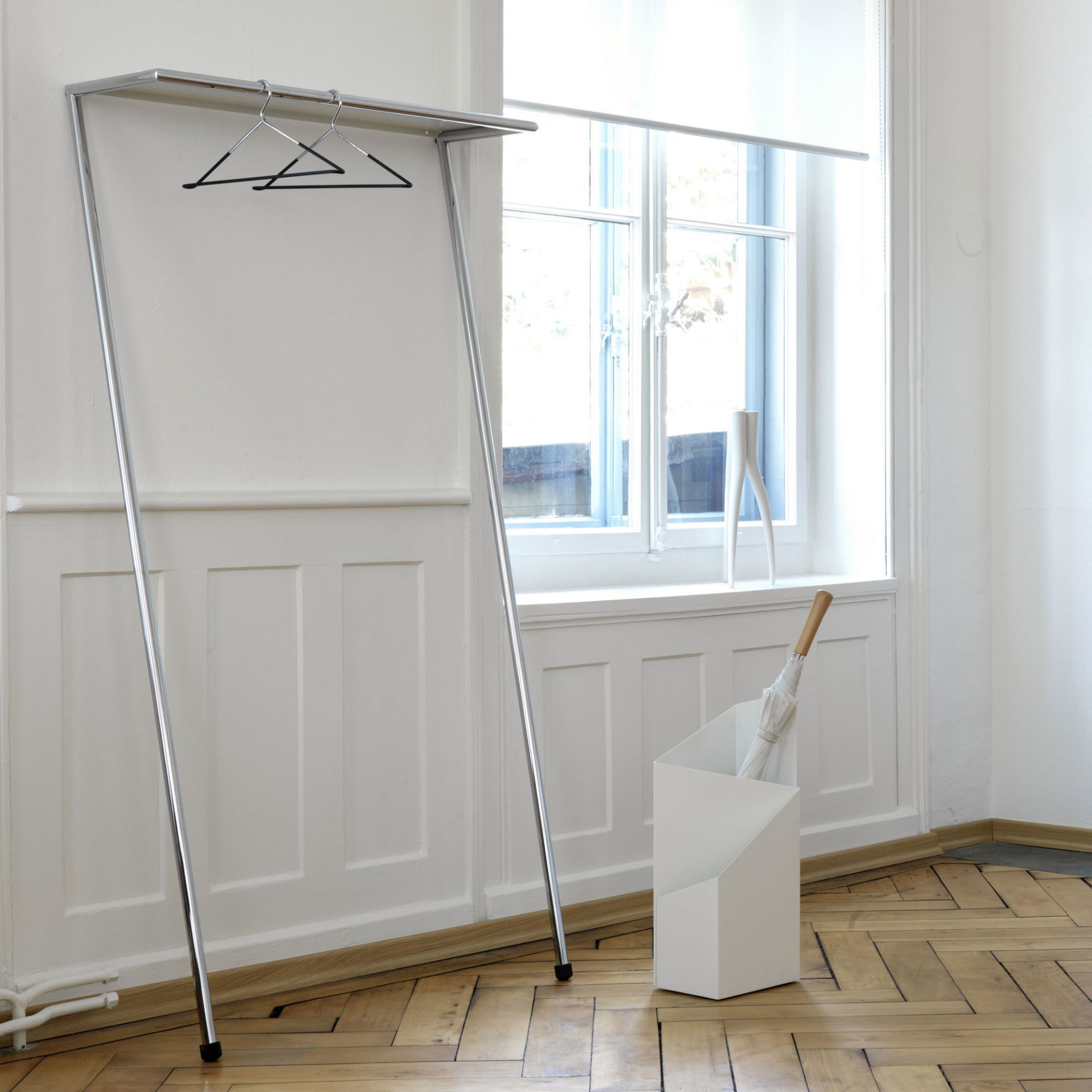 Zen Anlehngarderobe Mox in Chrom Glanz vor weißer Wand mit Kleiderbügeln und Schirmständer.