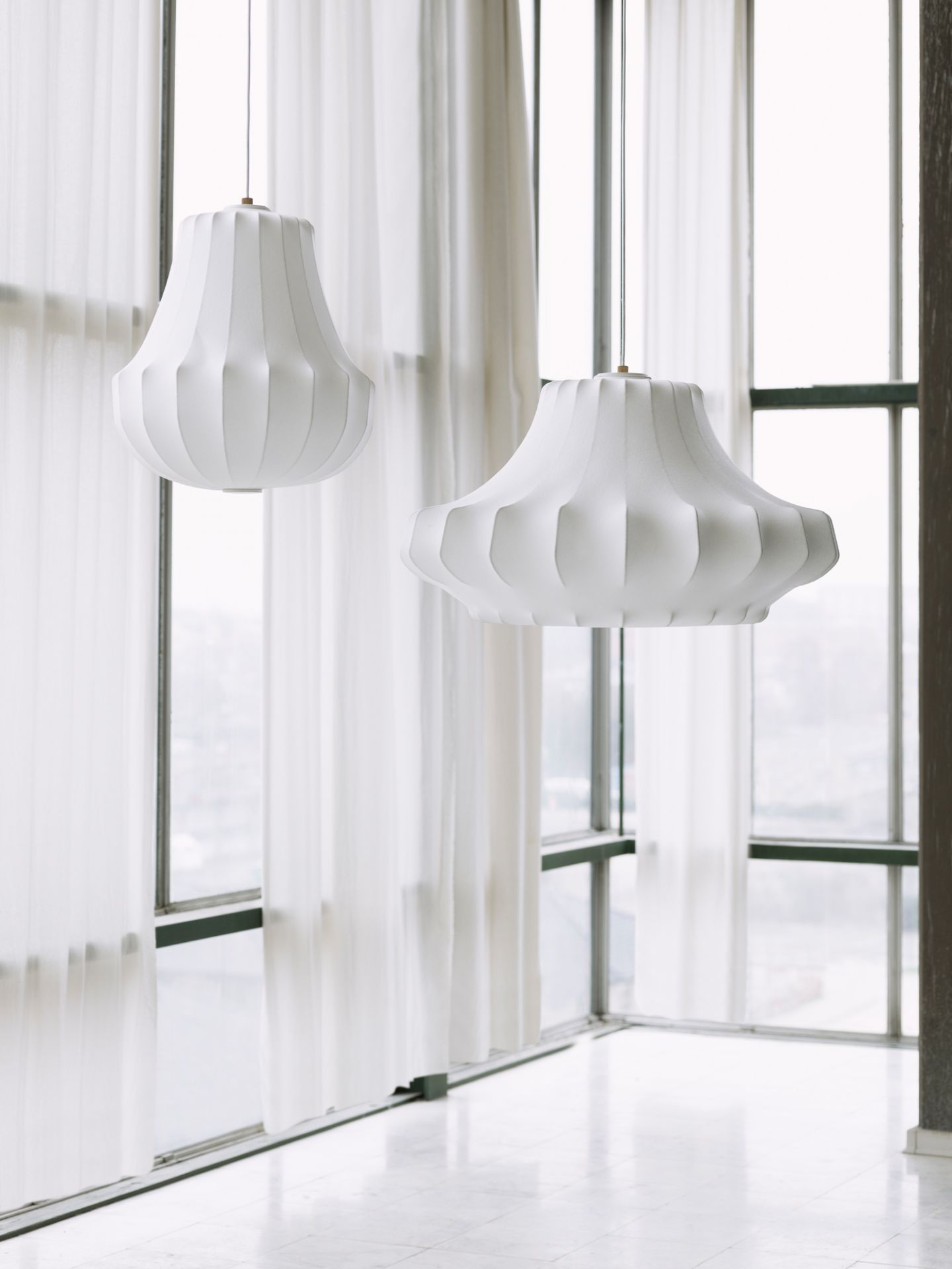 Zwei große, weiße Phantom Lamp Pendelleuchten von Normann Copenhagen vor einem Fenster.