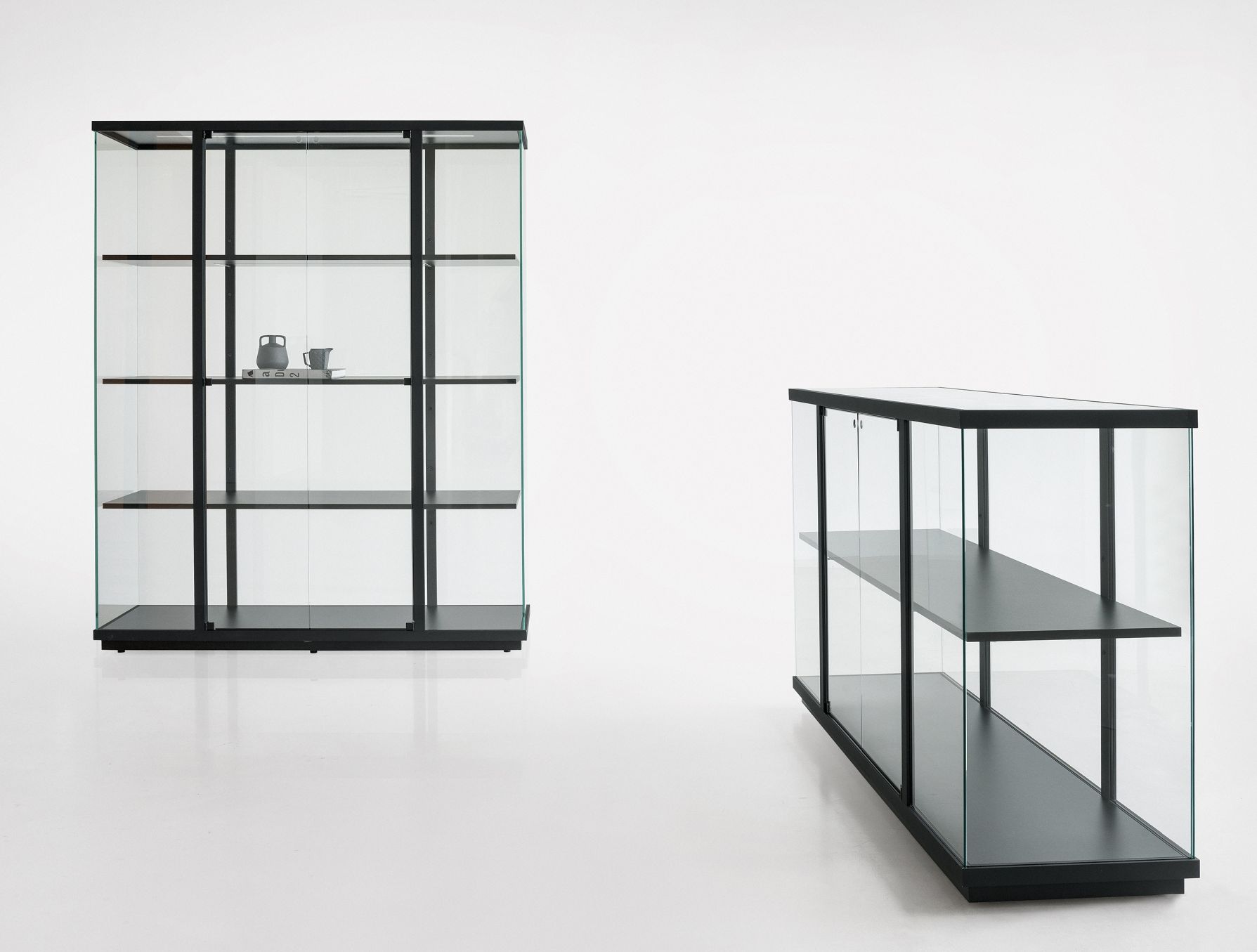 Zwei Stolp Vitrinen mit Glasfronten und schwarzen Rahmen, ideal für Wohnzimmer oder Ausstellungsräume.