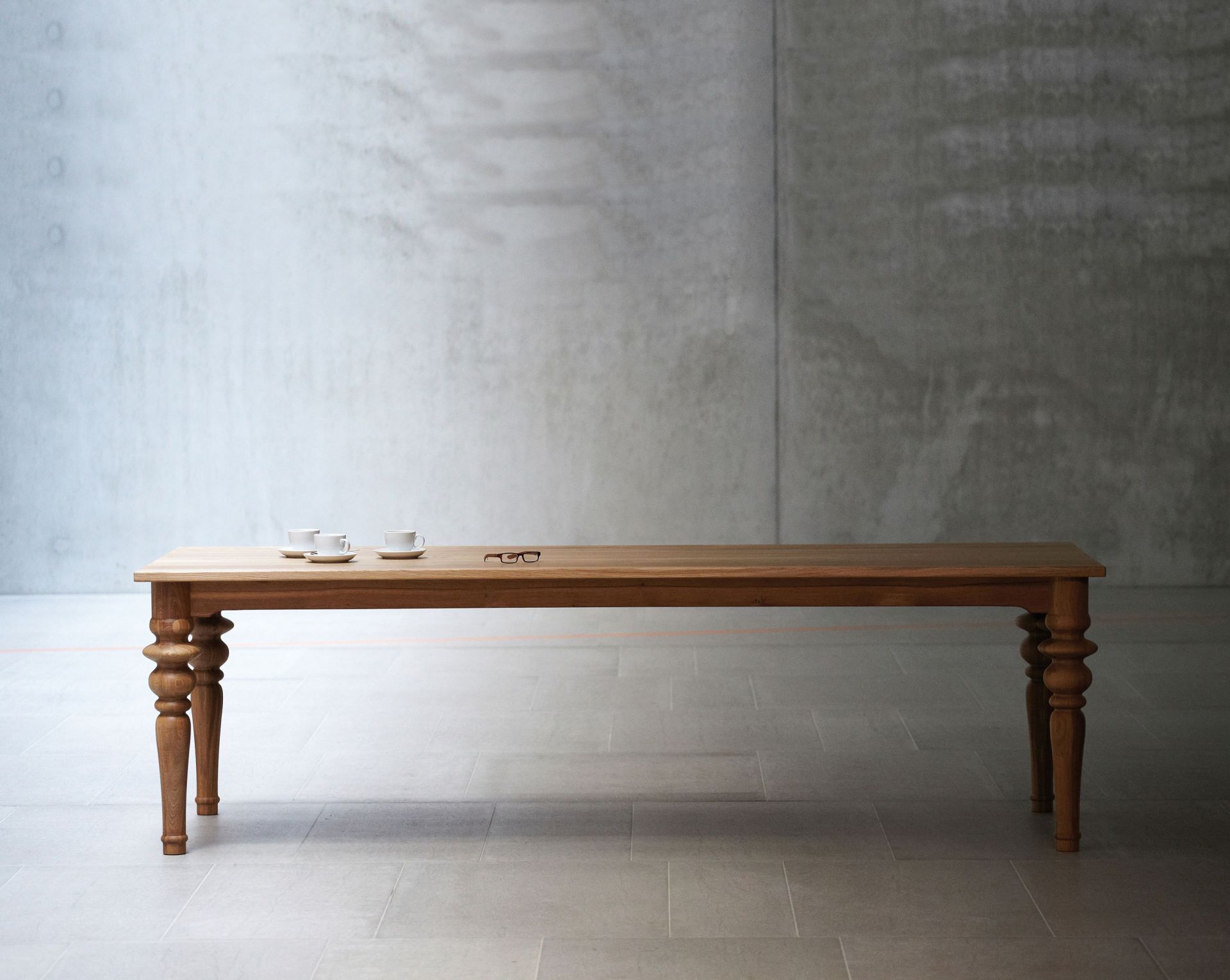Drexler Tisch von Jan Kurtz: Langer Holztisch mit gedrechselten Beinen, Kaffeetassen und Brille.