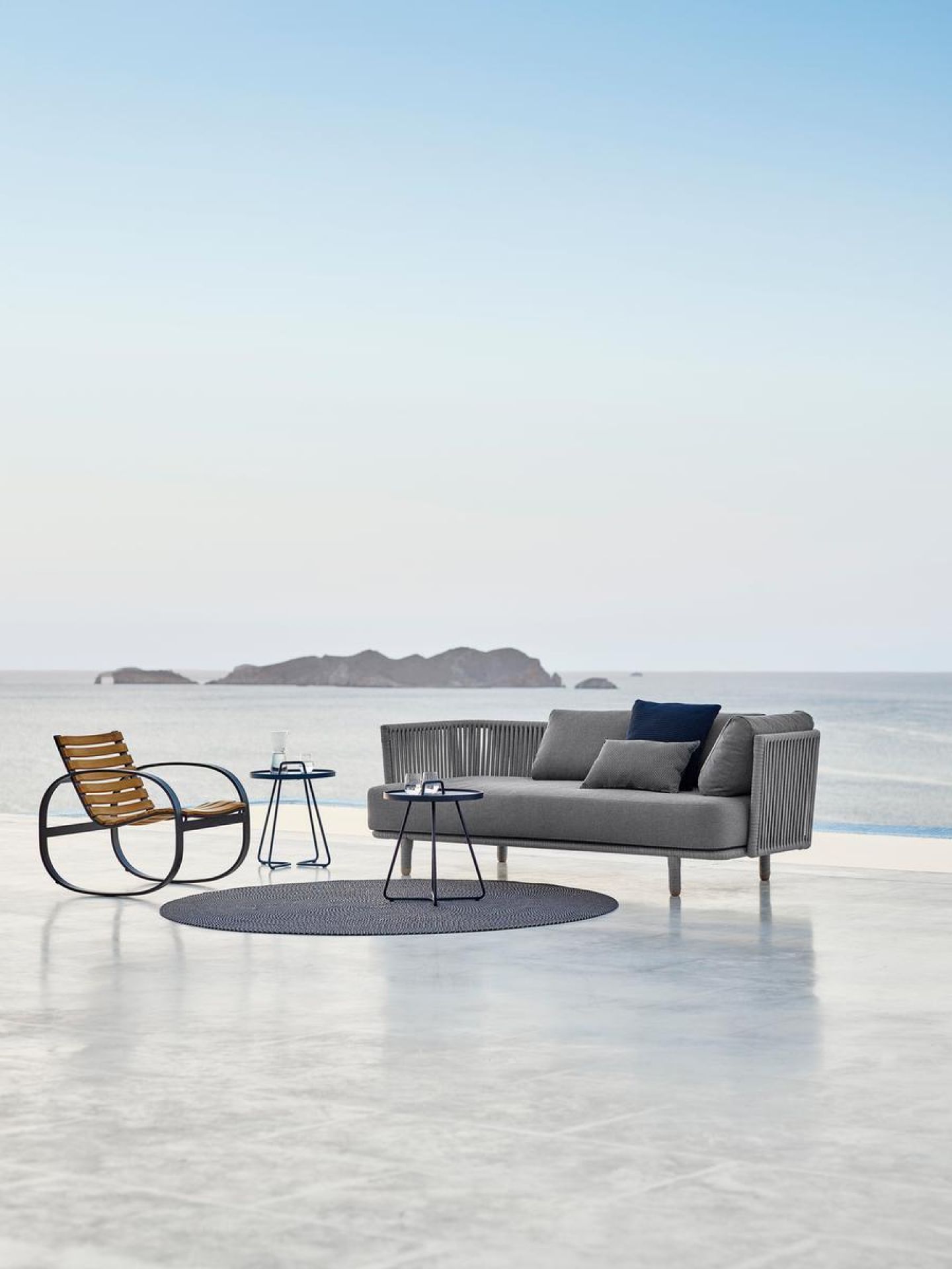 Cane-Line Moments Outdoor Sofa 3-Sitzer in Grau mit passendem Sessel und Beistelltischen.