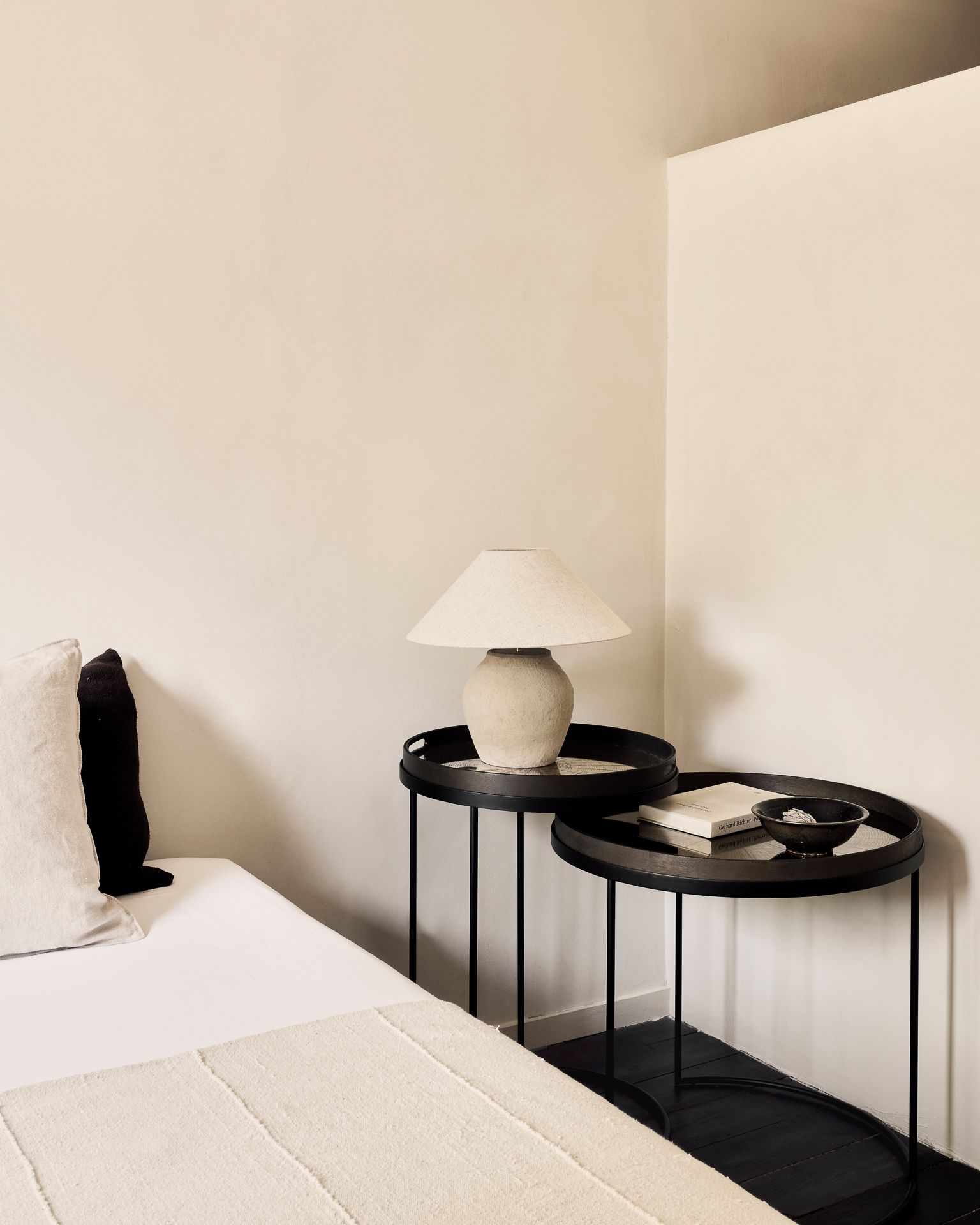 Ethnicraft Beistelltisch 2er Set Schwarz Rund: Zwei runde, schwarze Tische neben einem Bett.