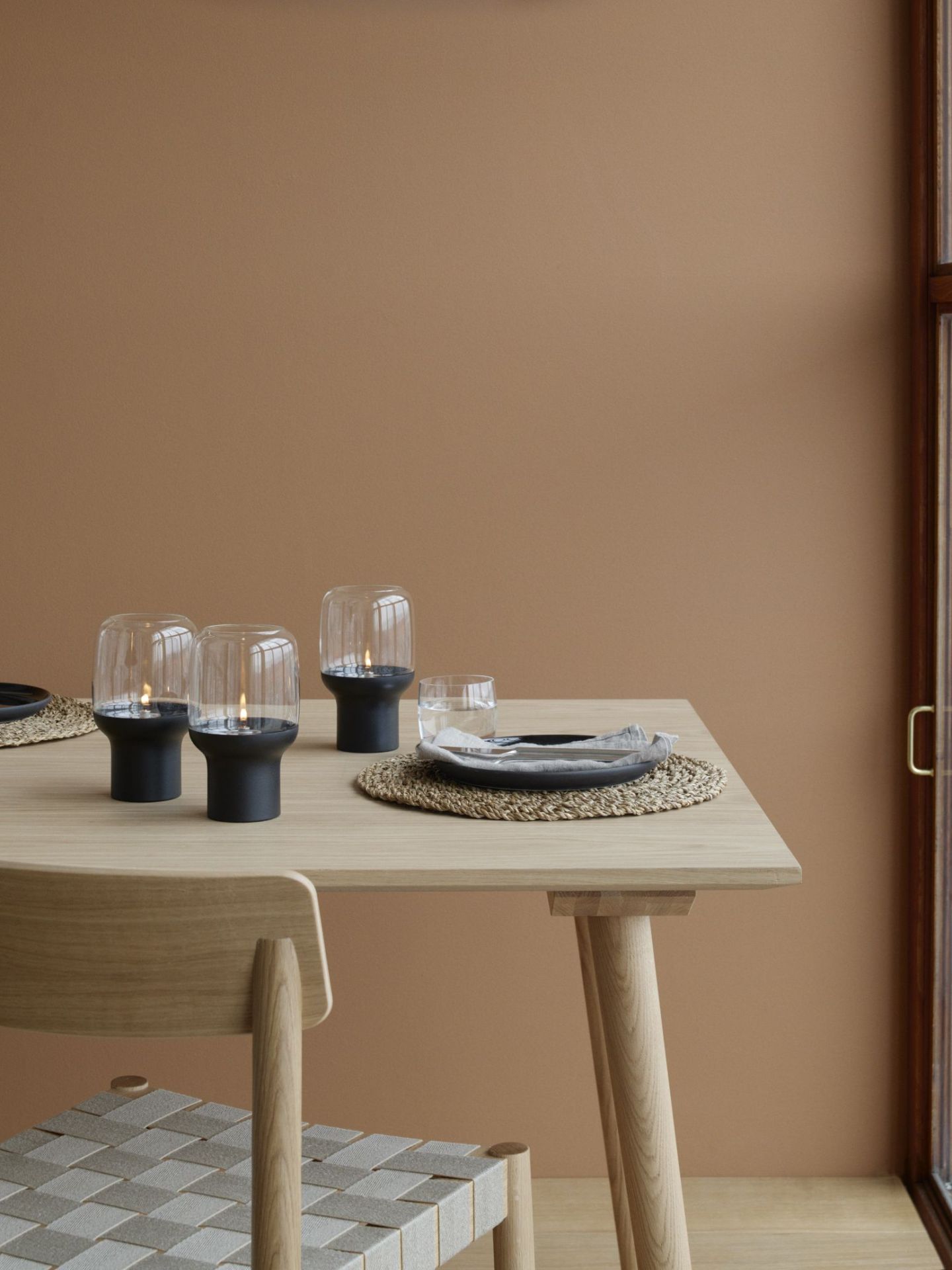 Tischdekoration mit Stelton Hoop Hurricane Windlichtern, Glas, Geschirr und Stuhl im minimalistischen Design.