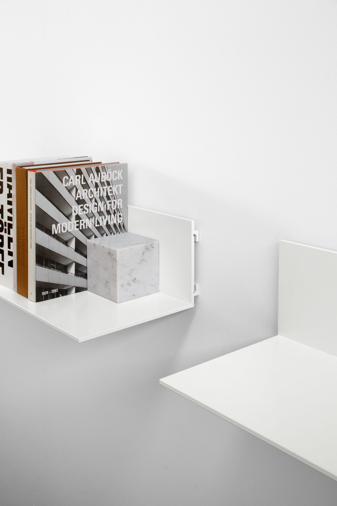 Weiße AC11 Stop Buchstütze von e15 mit Büchern und einem Marmor-Buchstützen-Würfel auf einer Wand.