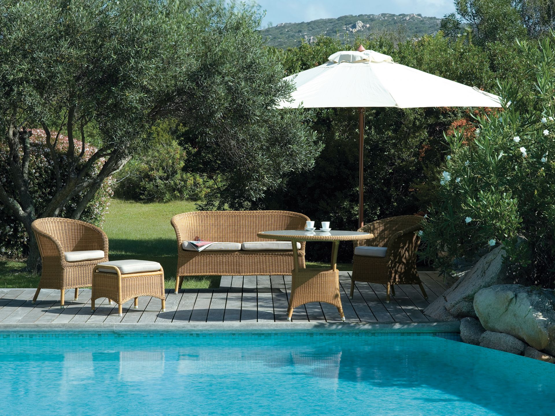 Derby Outdoor Sessel Cane-Line aus Rattan mit Sofa, Tisch und Sonnenschirm am Pool.