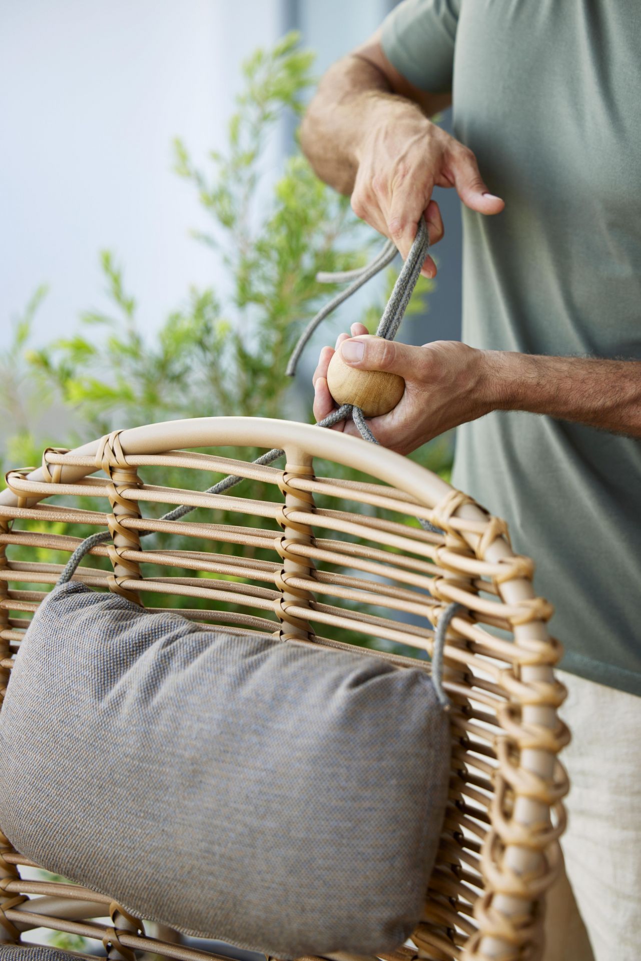 Mann befestigt Kissen am Cane-Line Hive Sessel aus Rattan mit Teakholz-Details.