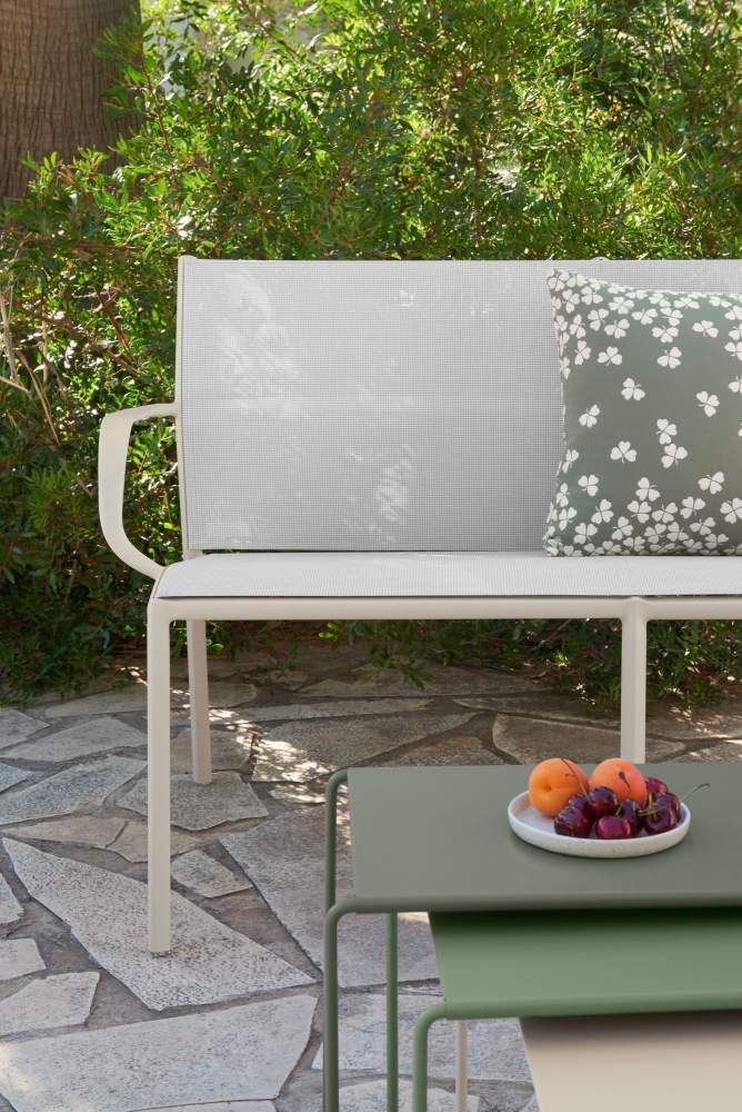 Cadiz Bank von Fermob: Weiße Gartenbank mit Kissen und Beistelltisch im Freien.