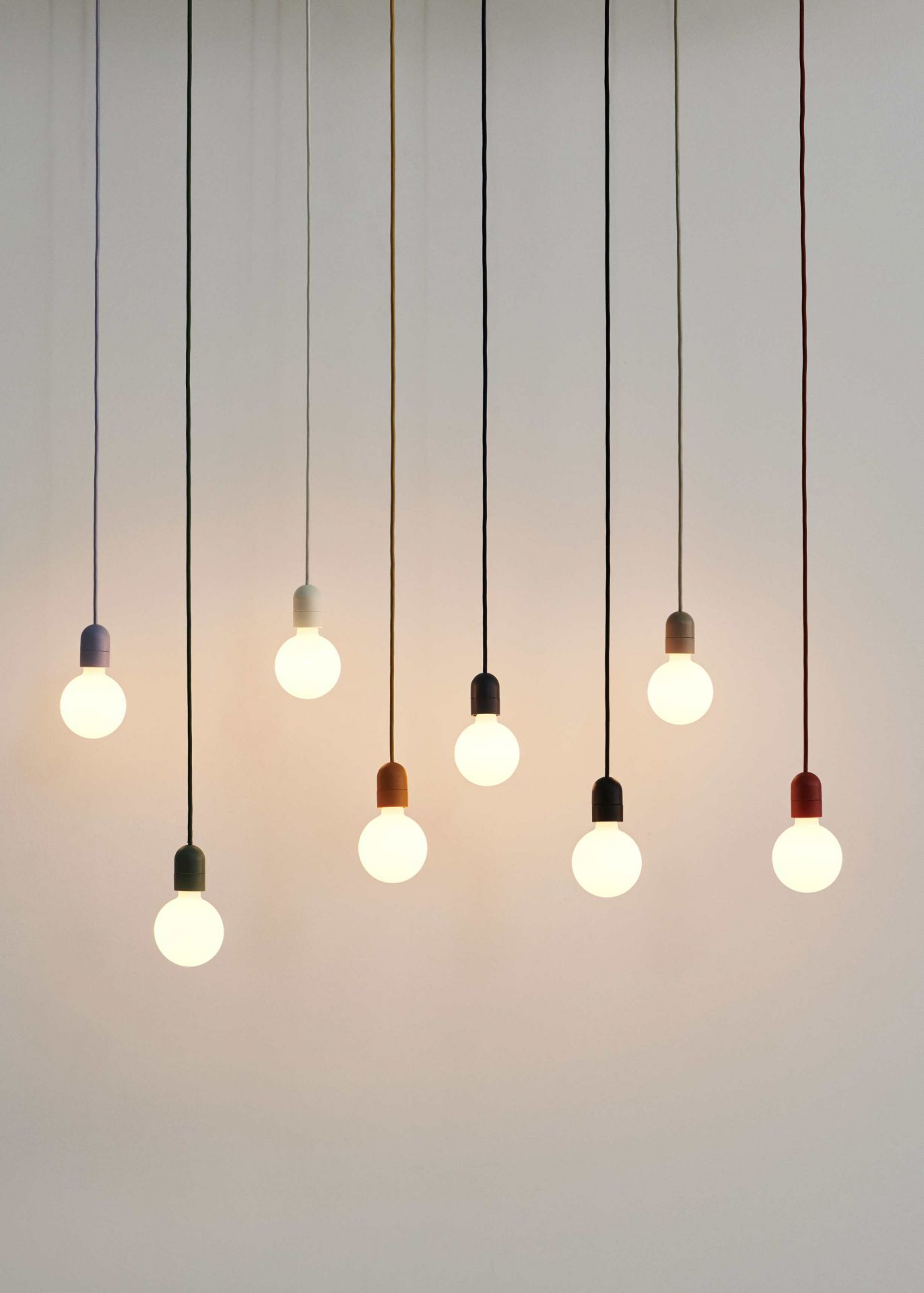 Mehrere Hay Pendelleuchten mit farbigen Textilkabeln und Glühbirnen vor hellem Hintergrund.