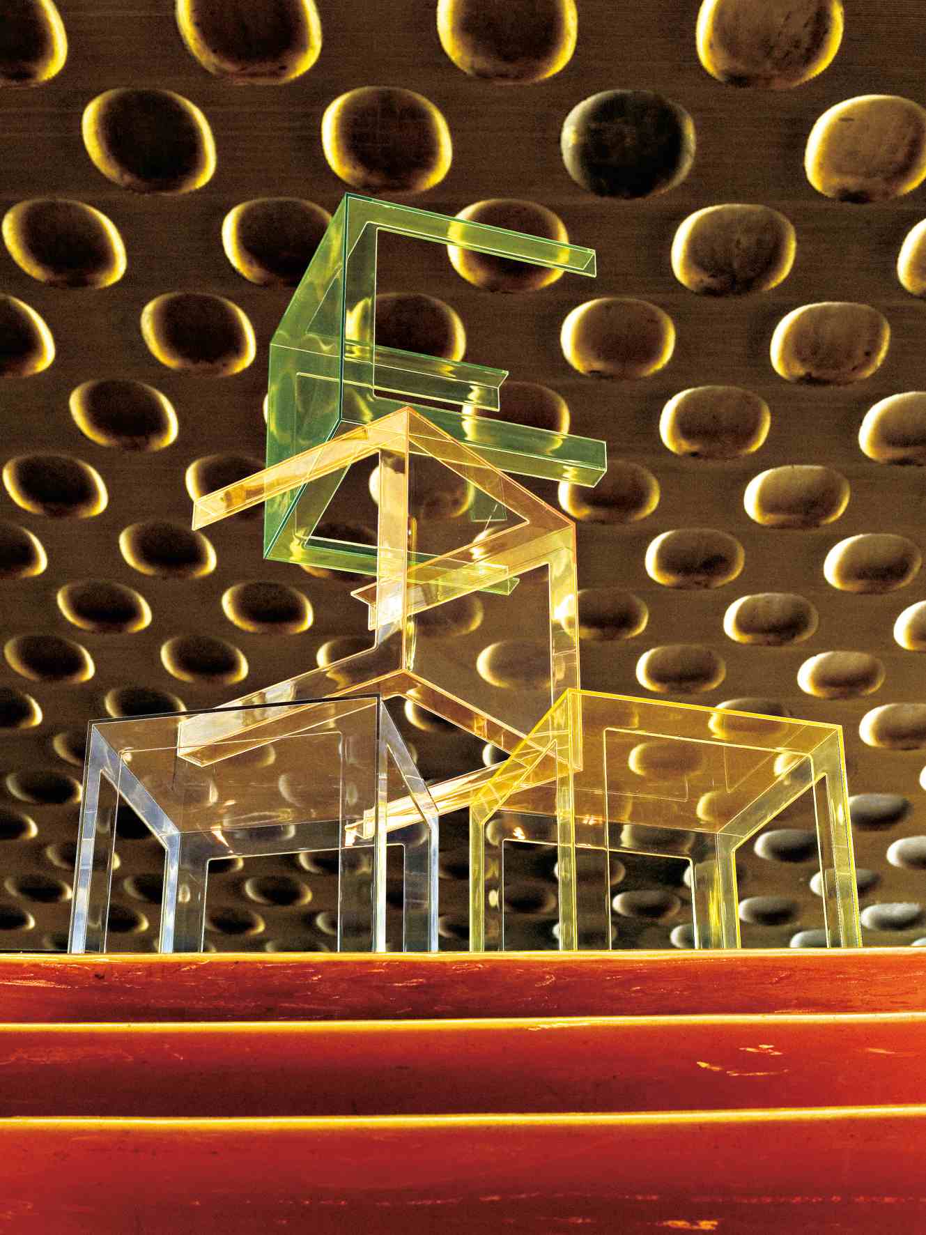 Stapel aus transparenten Jolly Beistelltischen von Kartell in verschiedenen Farben vor gemusterter Wand.