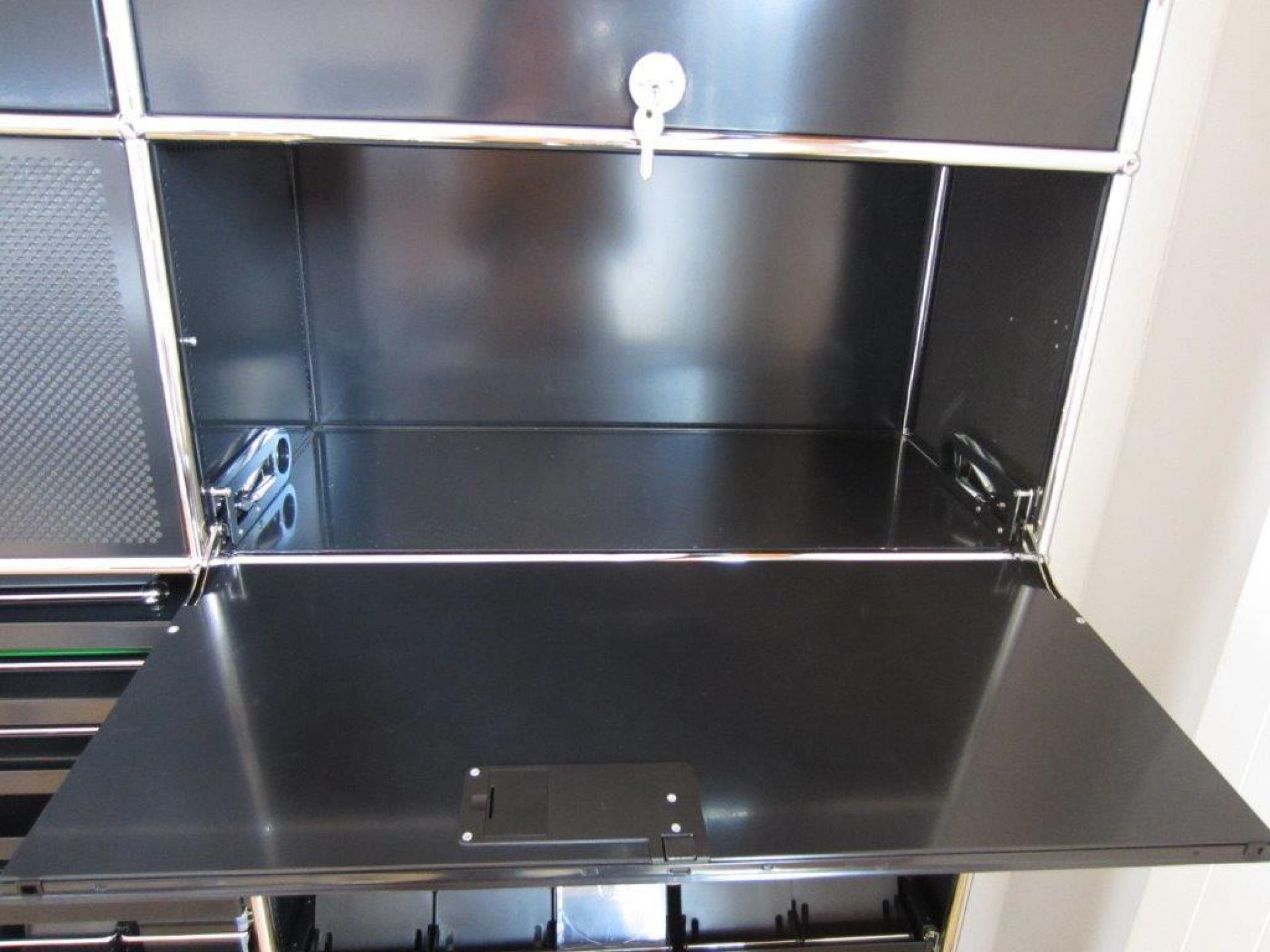 Detailaufnahme einer geöffneten stahlblauen USM Haller Klapptür als Ersatzteil, mit Schlüssel im Schloss.