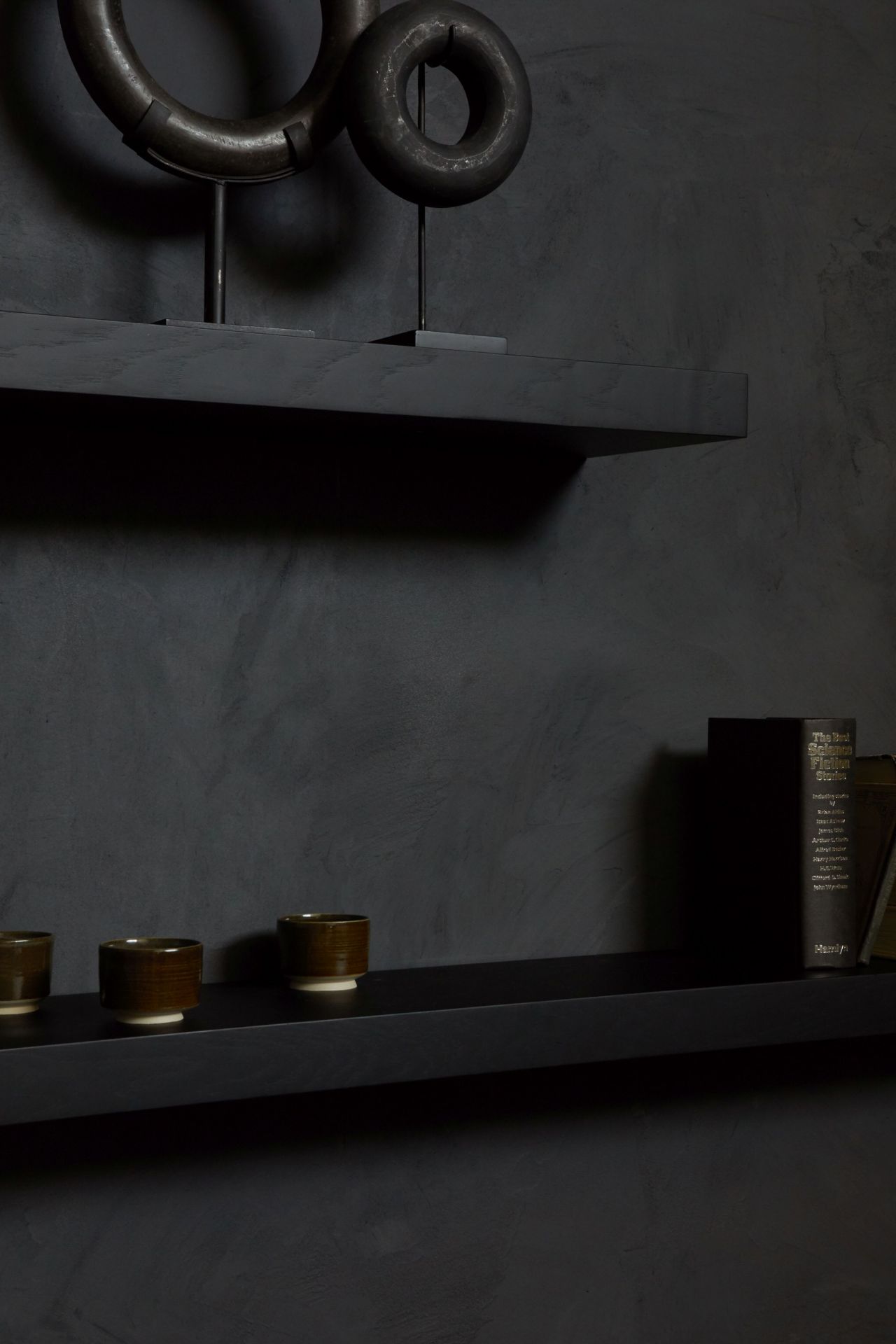 Schwarzes Ethnicraft Wandregal aus Eiche mit Deko-Objekten, Tassen und Buch vor dunkler Wand.