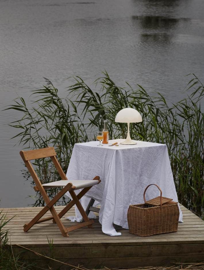 Panthella Tischleuchte 250 LED von Louis Poulsen in Opal Pale rosa auf gedecktem Tisch am See.