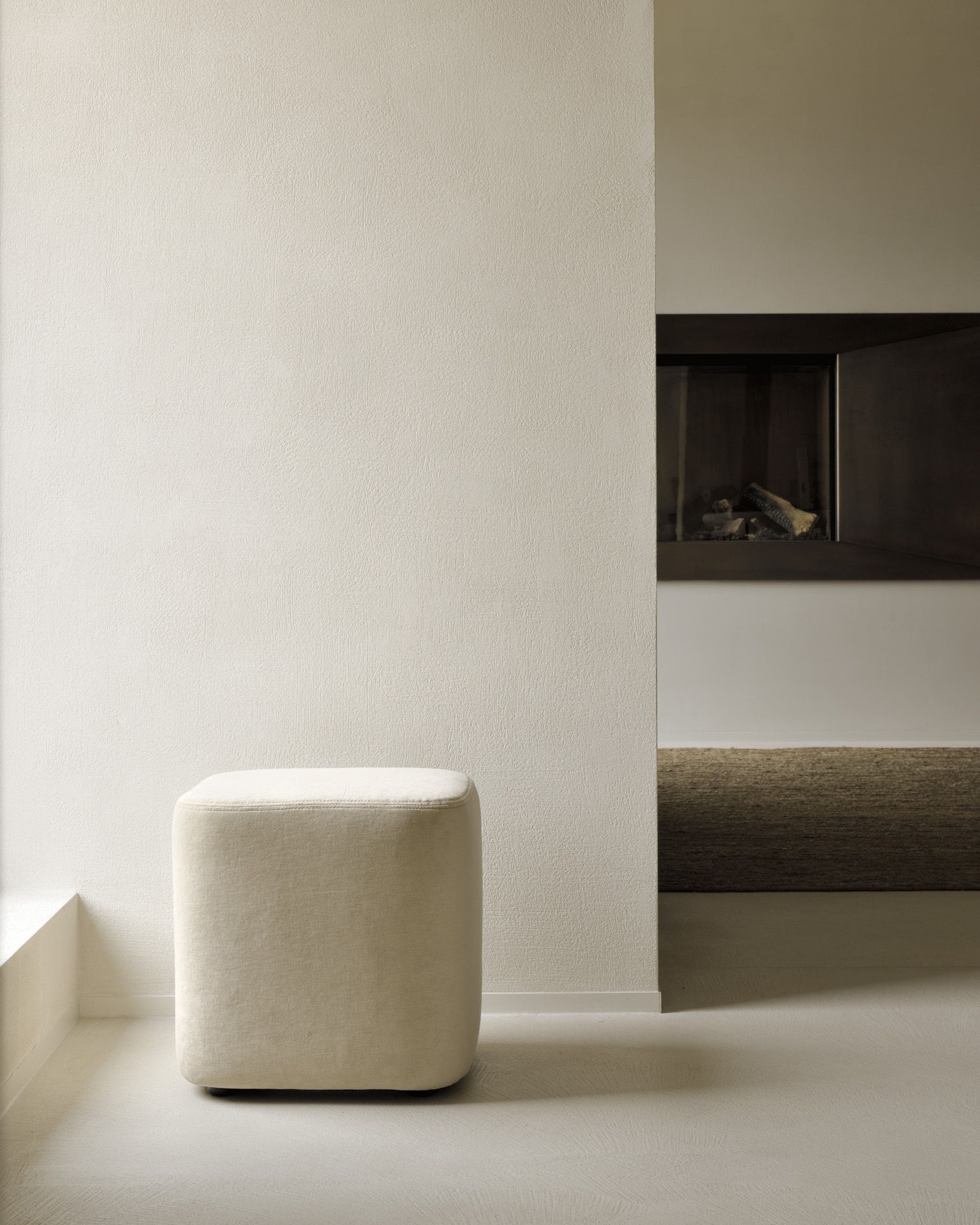 Beiger Cube Pouf Sitzhocker von Ethnicraft im minimalistischen Interieur mit Kamin. Modernes Wohnaccessoire.