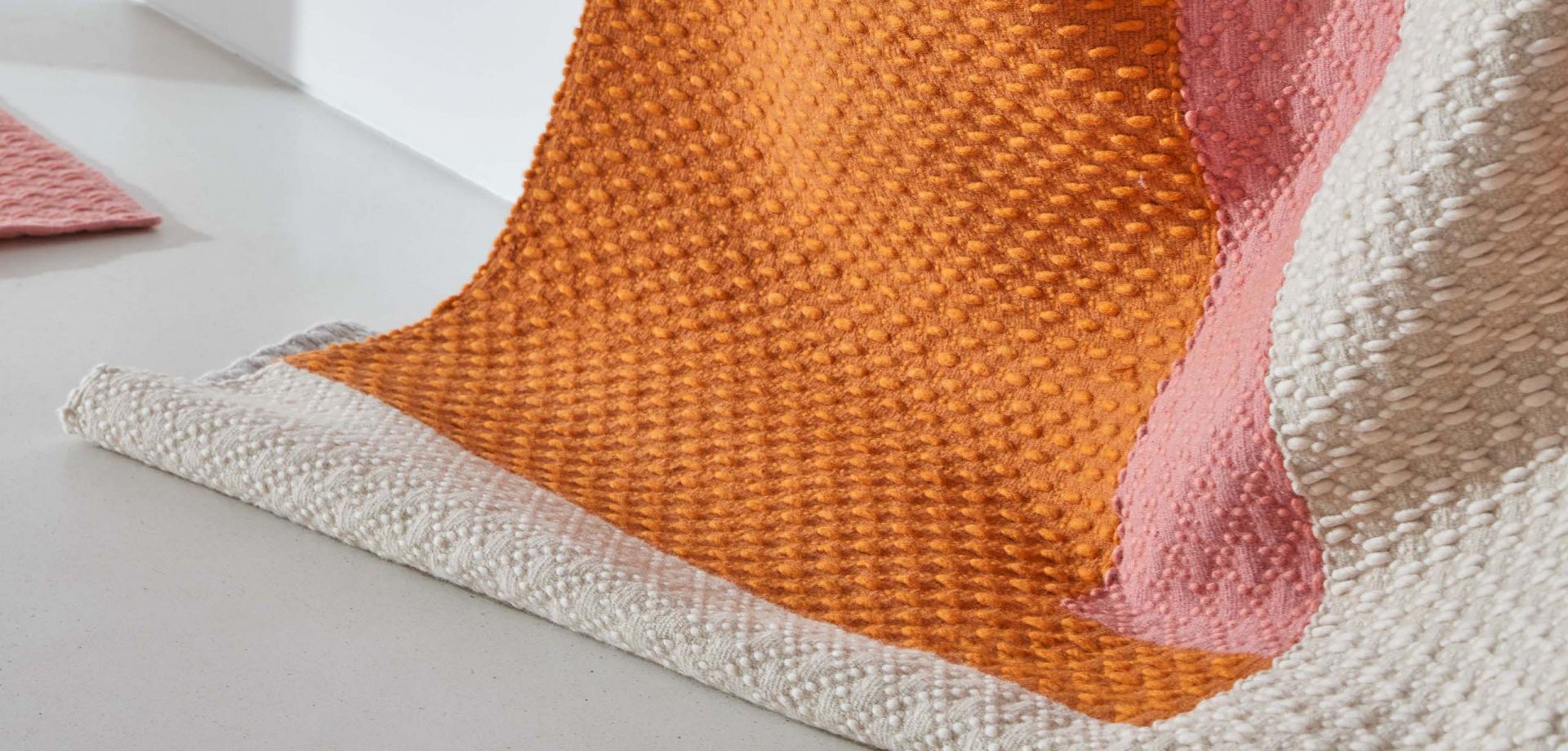 Detailaufnahme des Space Hopper Teppichs in Orange, Rosa und Beige mit gewebter Textur.