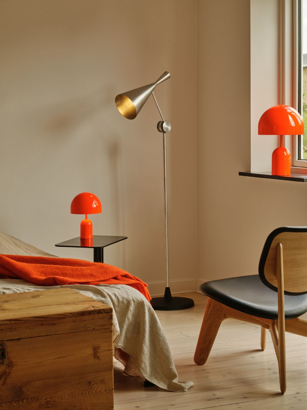 Moderne Unbeaten Stehleuchte von Tom Dixon im Schlafzimmer, ergänzt durch orangefarbene Tischlampen und einen Holzstuhl.