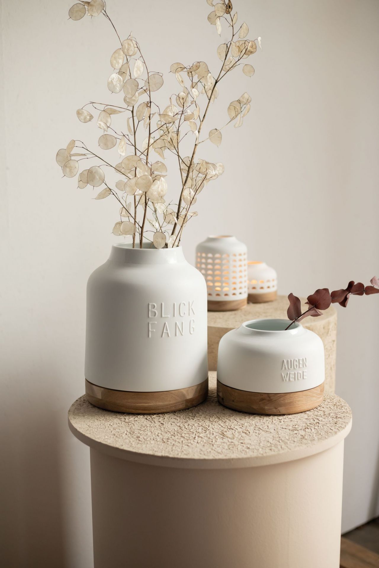 Weiße Räder Vasen "Blickfang" und "Augenweide" mit Holzfuß und Trockenblumen auf beigem Tisch.