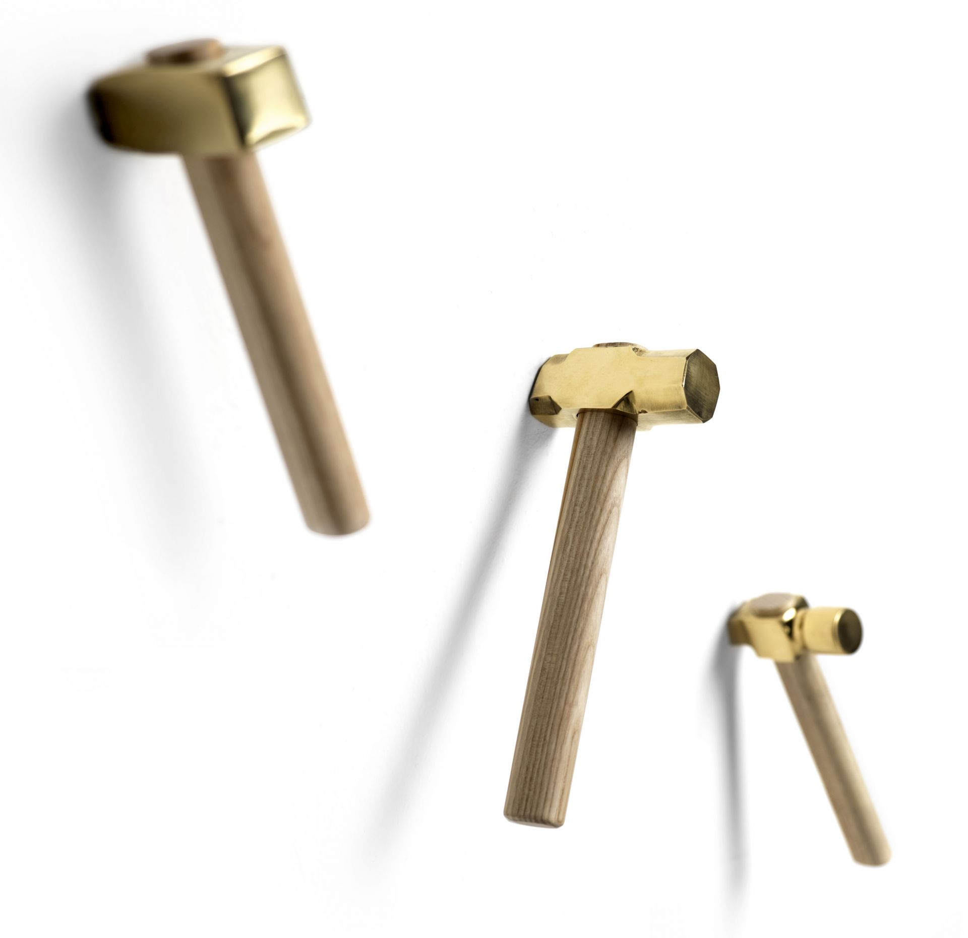 Drei Bastaaa Kleiderhaken im Hammer Design aus Holz und Messing an einer weißen Wand.