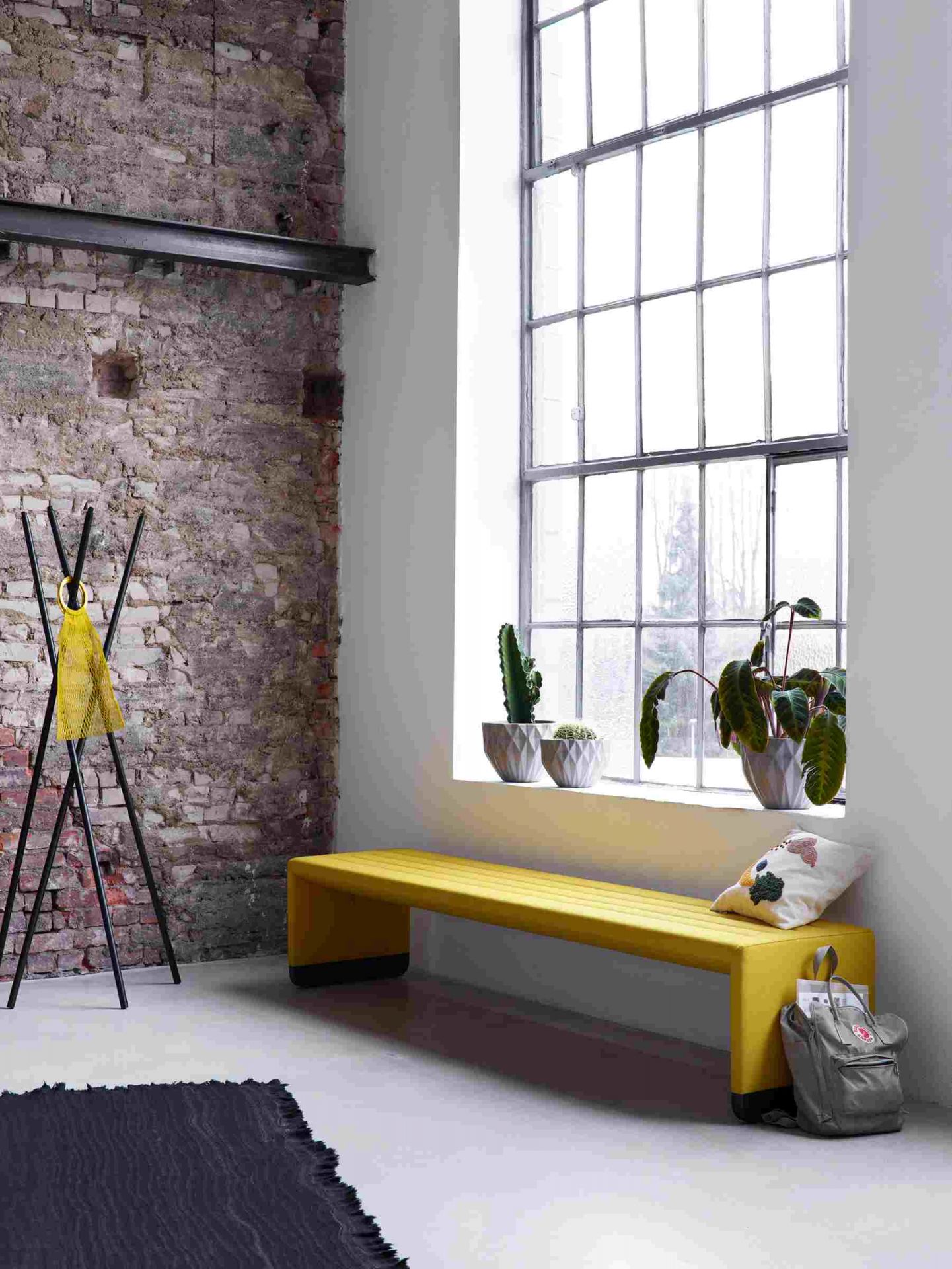 Gelbe Cor Bridge Polsterbank im Loft-Stil mit Zierkissen und Pflanzen am Fenster.