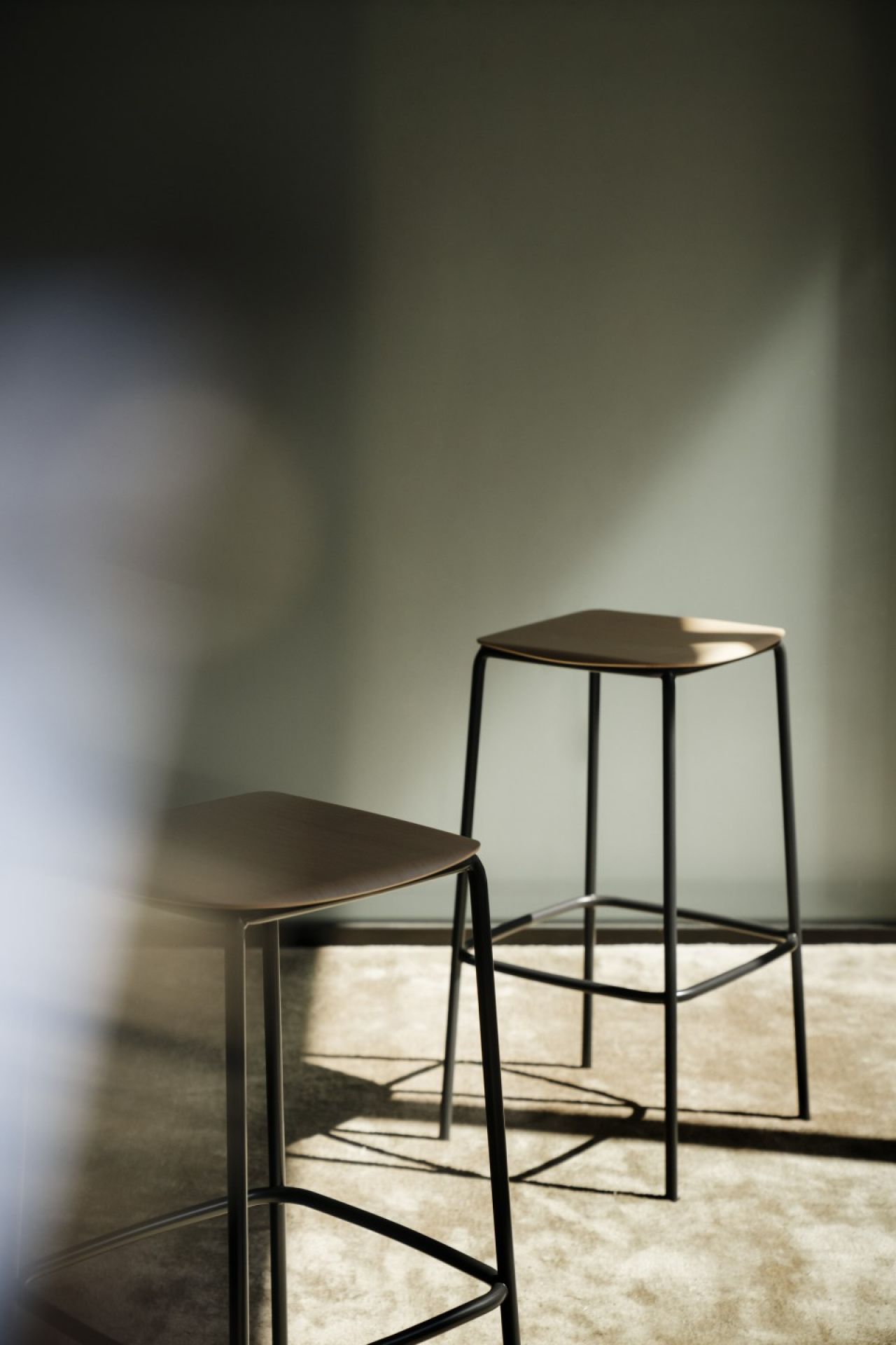 Zwei Nate Barhocker von Brunner mit Holzsitzen und schwarzem Metallgestell im Detail.