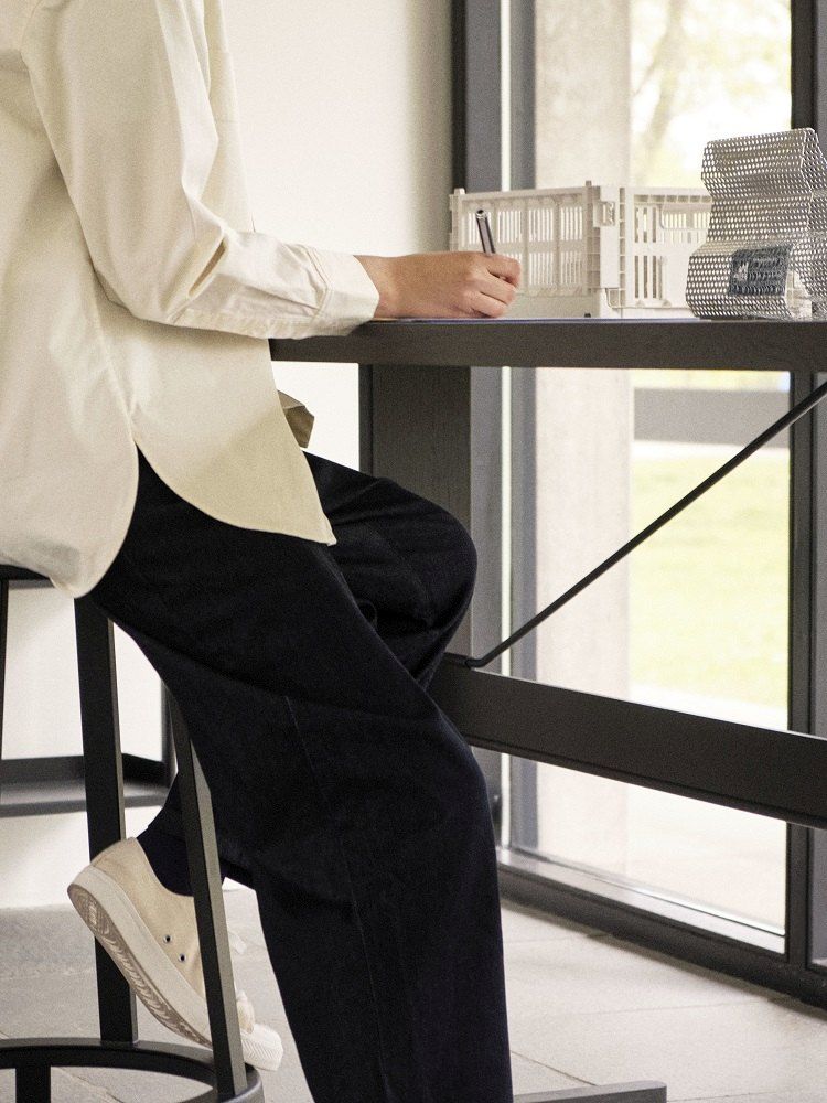 Person sitzt am Passerelle High Table Stehtisch mit schwarzem Gestell und arbeitet.