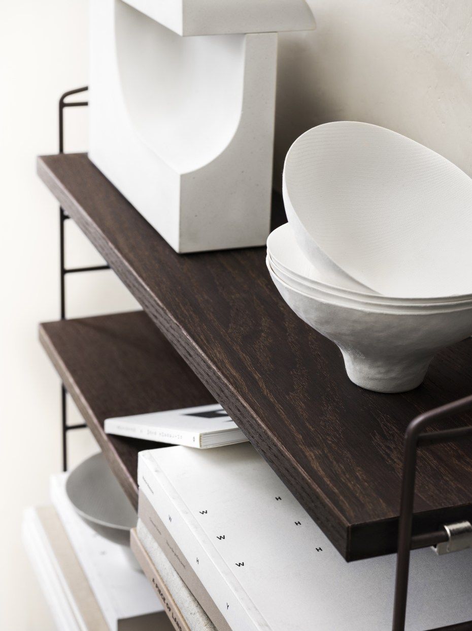 Nahaufnahme eines String Furniture Regalsystems mit dunklen Holzregalen und dekorativen Objekten.