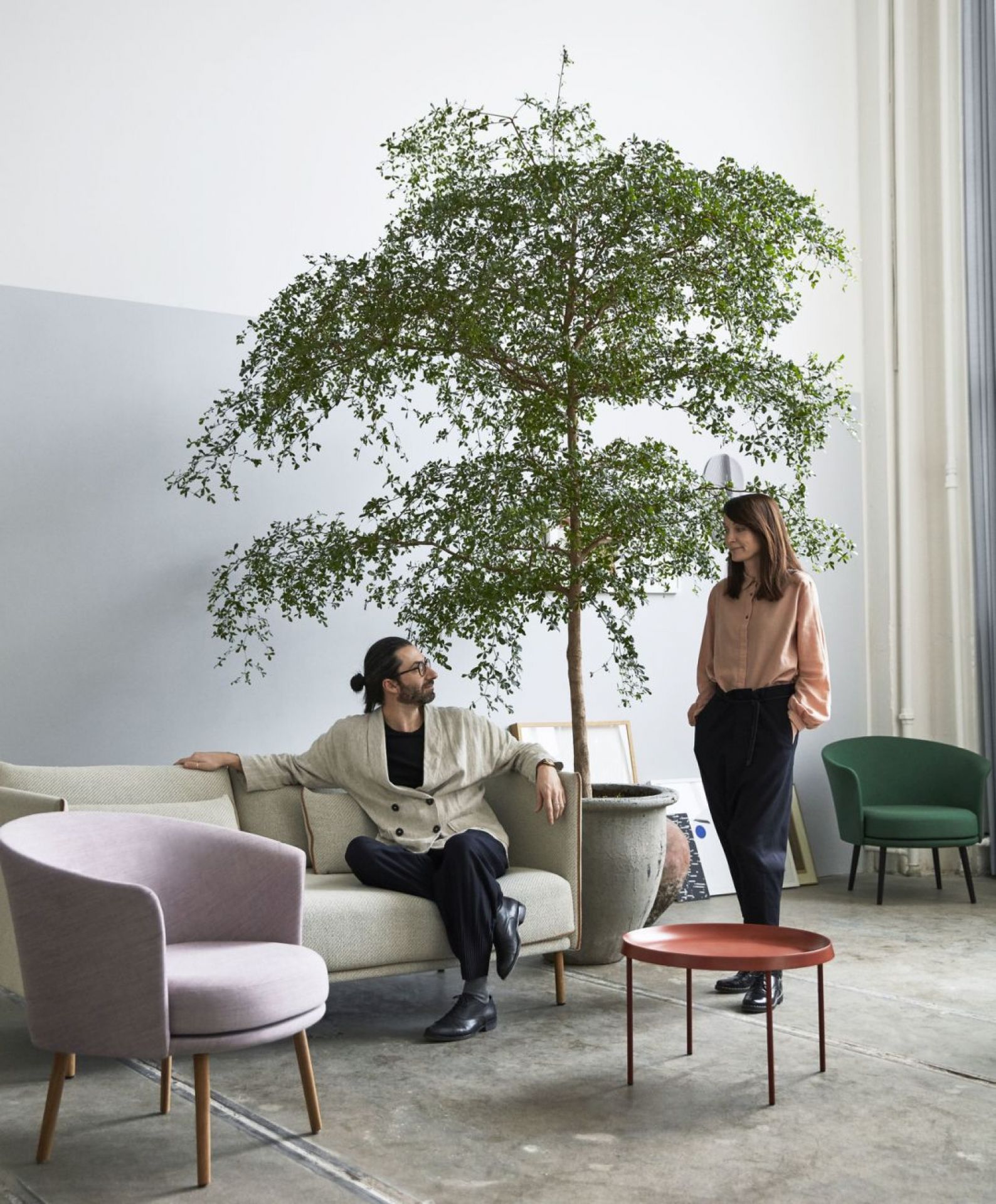 Wohnzimmer mit Hay Dorso Loungesessel in Lila und Grün, Sofa, Tisch und Personen.