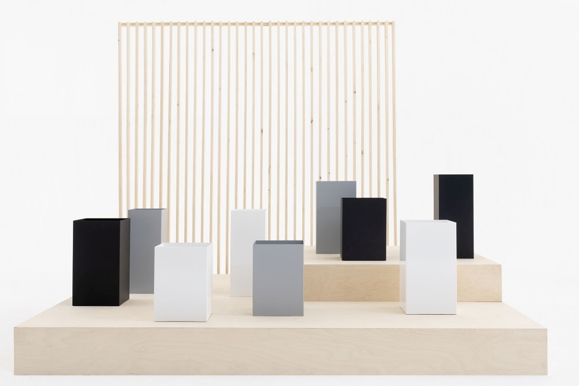 Quadratische Cascando Papierkörbe in Schwarz, Weiß und Grau auf einer Holzplattform. Design Papierkorb.