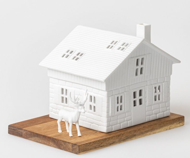 Lichthaus Skihütte: Weißes Keramikhaus mit Fensteröffnungen und kleinem Reh auf Holzsockel.