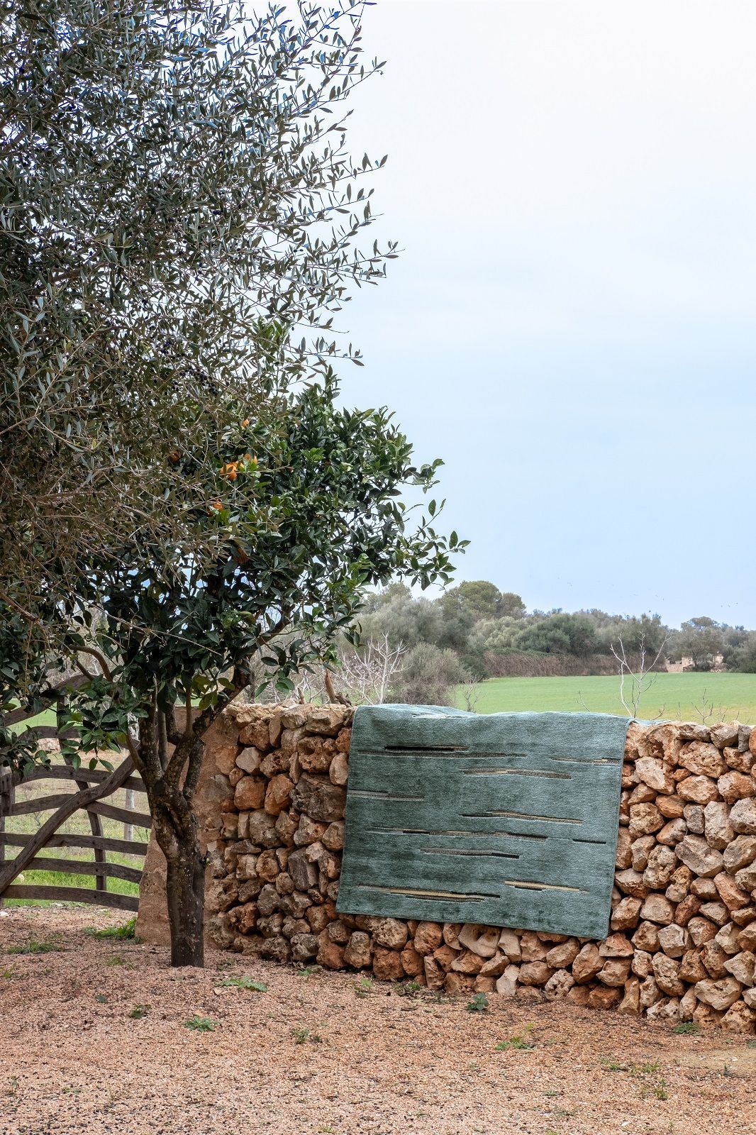 Colorado Teppich von Nanimarquina, grüner Wollteppich mit horizontalen Linien an einer Steinmauer.