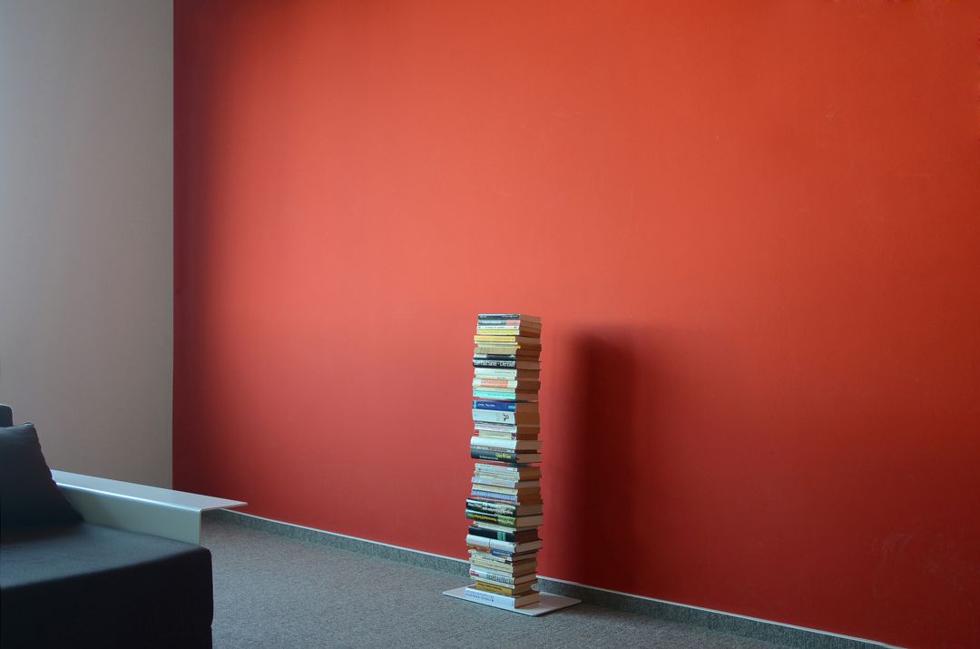 Booksbaum Standregal: Bücherstapel als kreatives Regal vor roter Wand. Bücherregal, Designmöbel.