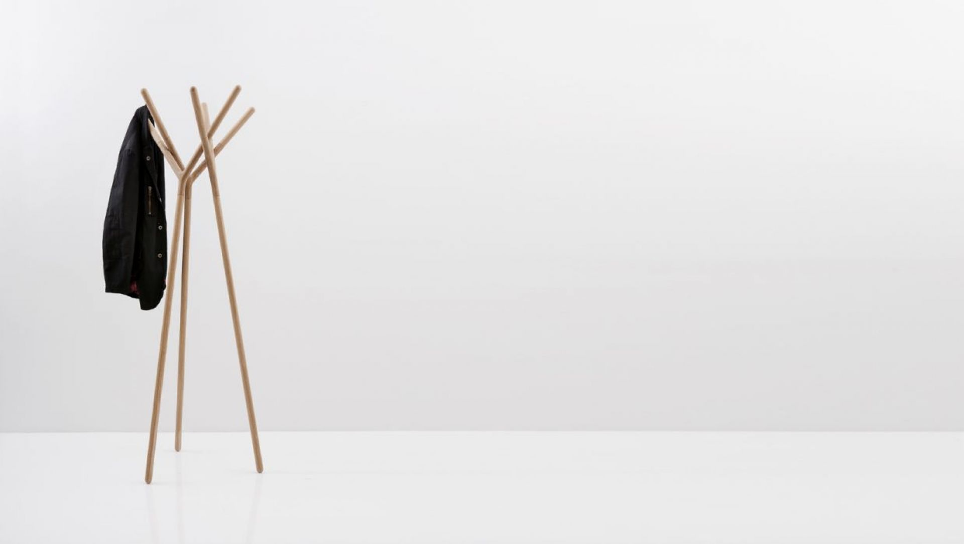 Game of Trust Garderobenständer von Miniforms aus hellem Holz mit einer schwarzen Jacke.