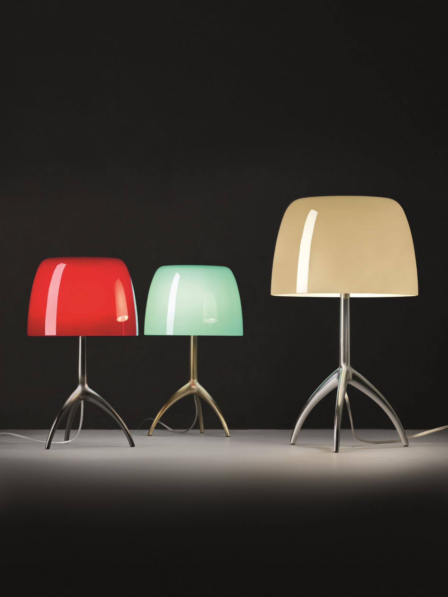 Drei Foscarini Lumiere Piccola Tischleuchten in Rot, Grün und Beige mit Stativfuß.