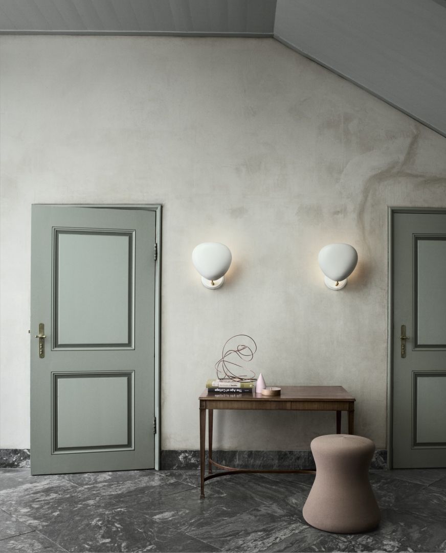 Zwei matte, weiße Cobra Wandleuchten von Gubi beleuchten einen Flur mit Tisch und Hocker.