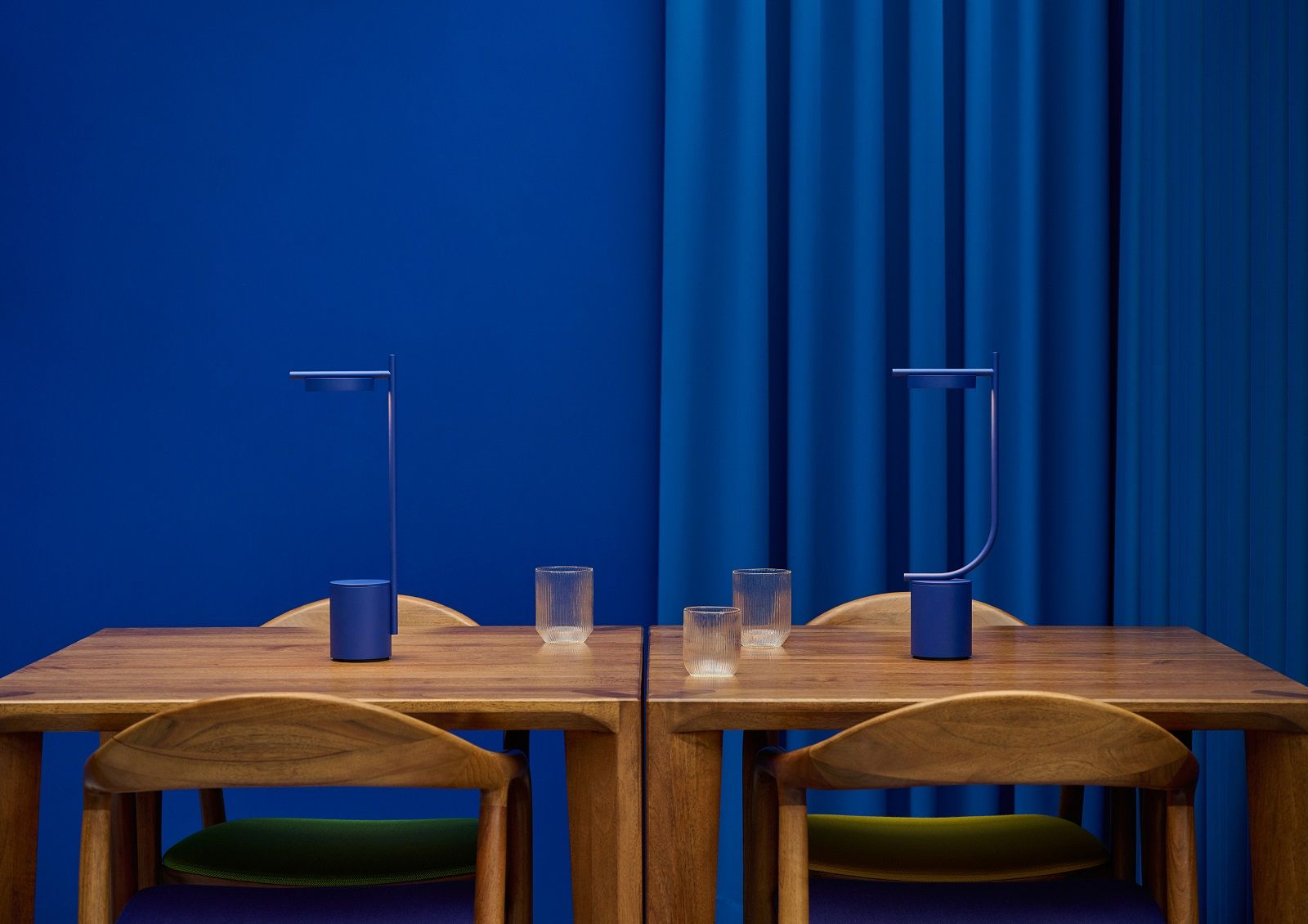 Blaue Igram Tischleuchte von Grupa auf Holztisch mit Gläsern und Stühlen.