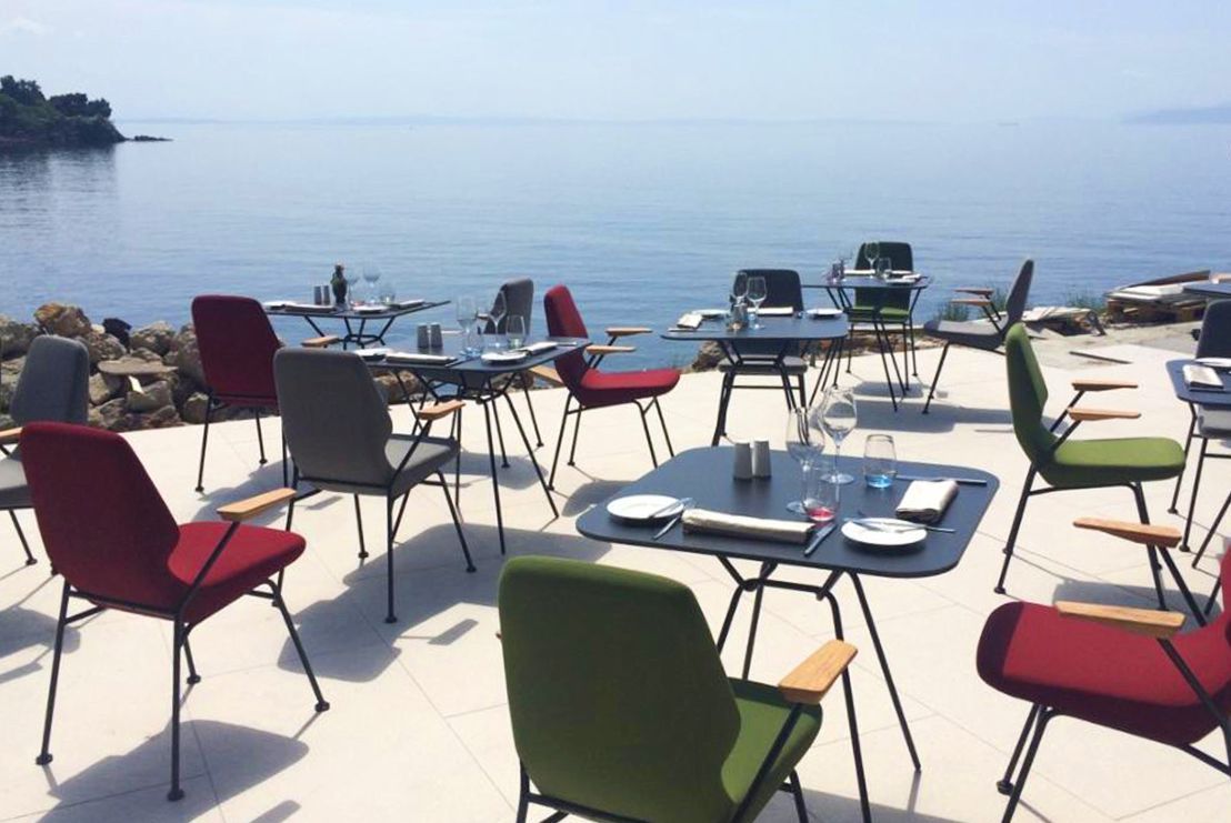 Mehrere Prostoria Oblique Sessel in Rot, Grau und Grün im Außenbereich mit Meerblick.