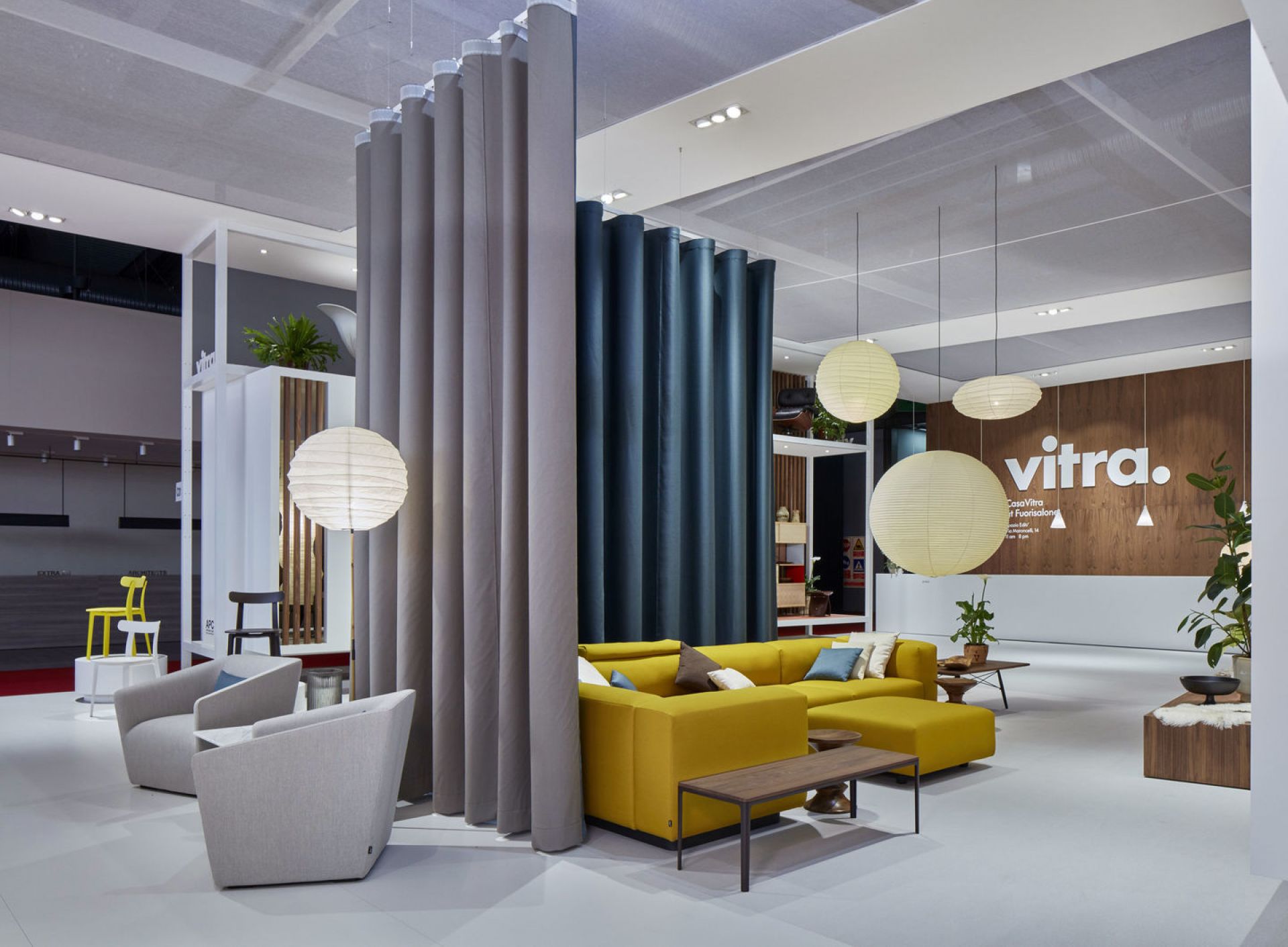 Innenraum mit Akari Pendelleuchten von Vitra, gelbem Sofa und grauen Sesseln.