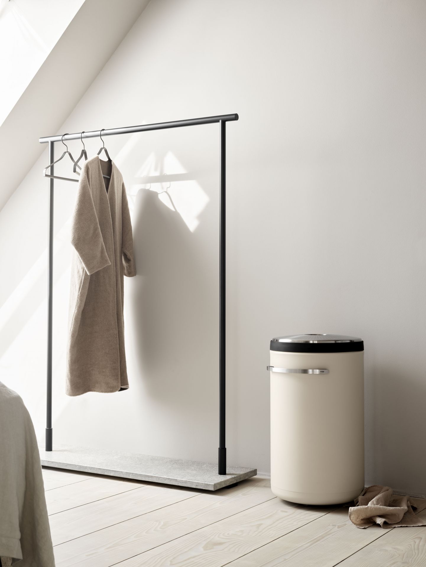 Beiger Vipp Wäschekorb im minimalistischen Schlafzimmer neben Kleiderständer und hellem Holzboden.