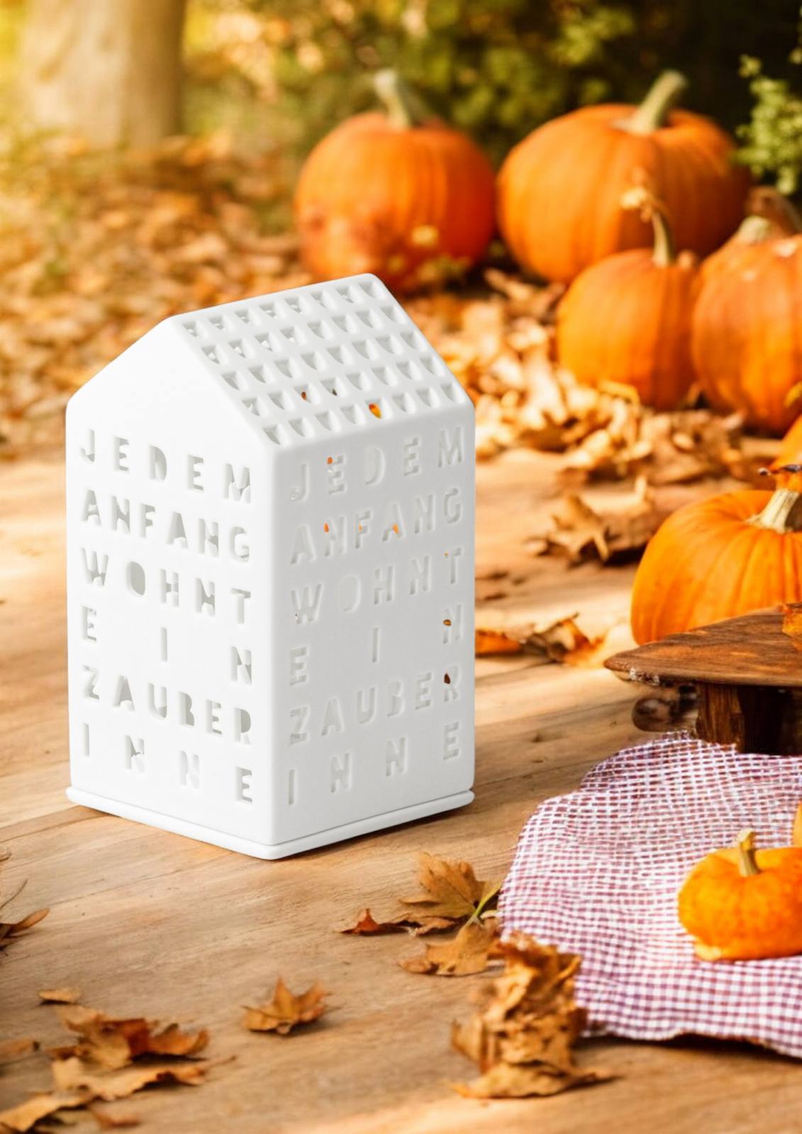 Weißes Räder Lichthaus "Jedem Anfang wohnt ein Zauber inne" mit Kürbissen und Herbstlaub.