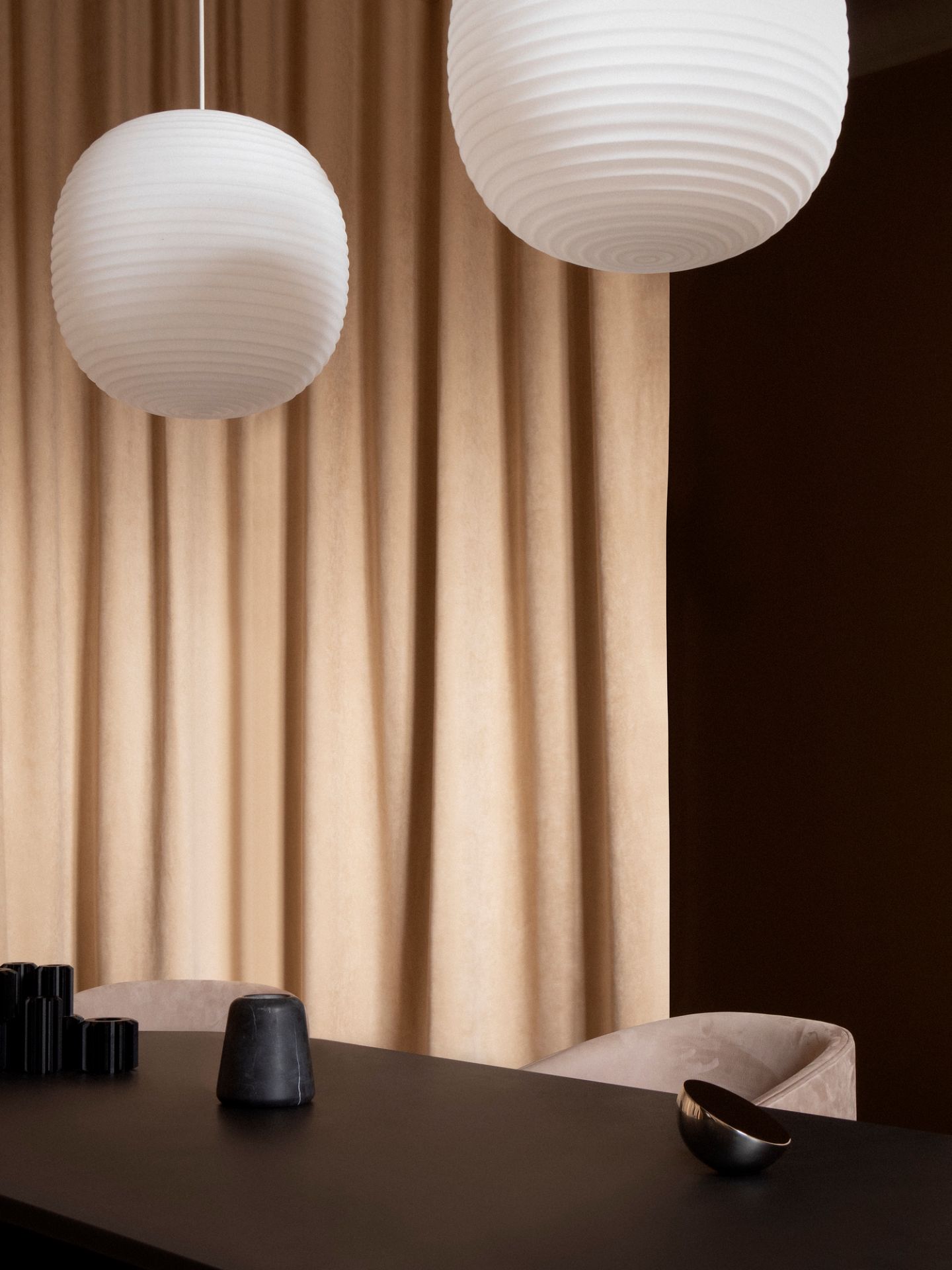 Nahaufnahme von zwei weißen Lantern Pendelleuchten von New Works über einem Esstisch.