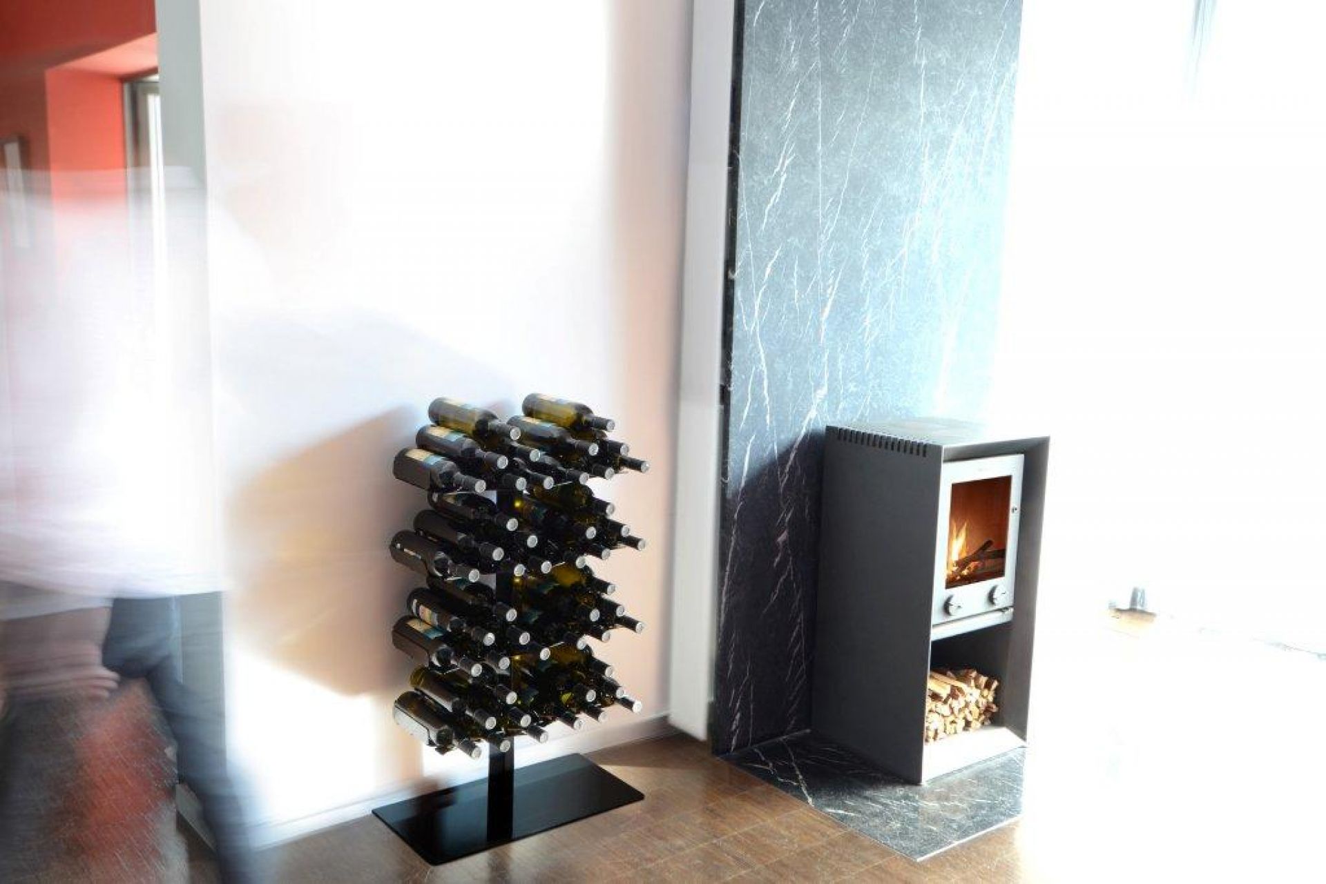 Wine Tree Weinregal Radius aus Metall, stehend im Wohnzimmer neben einem Kamin, gefüllt mit Weinflaschen.