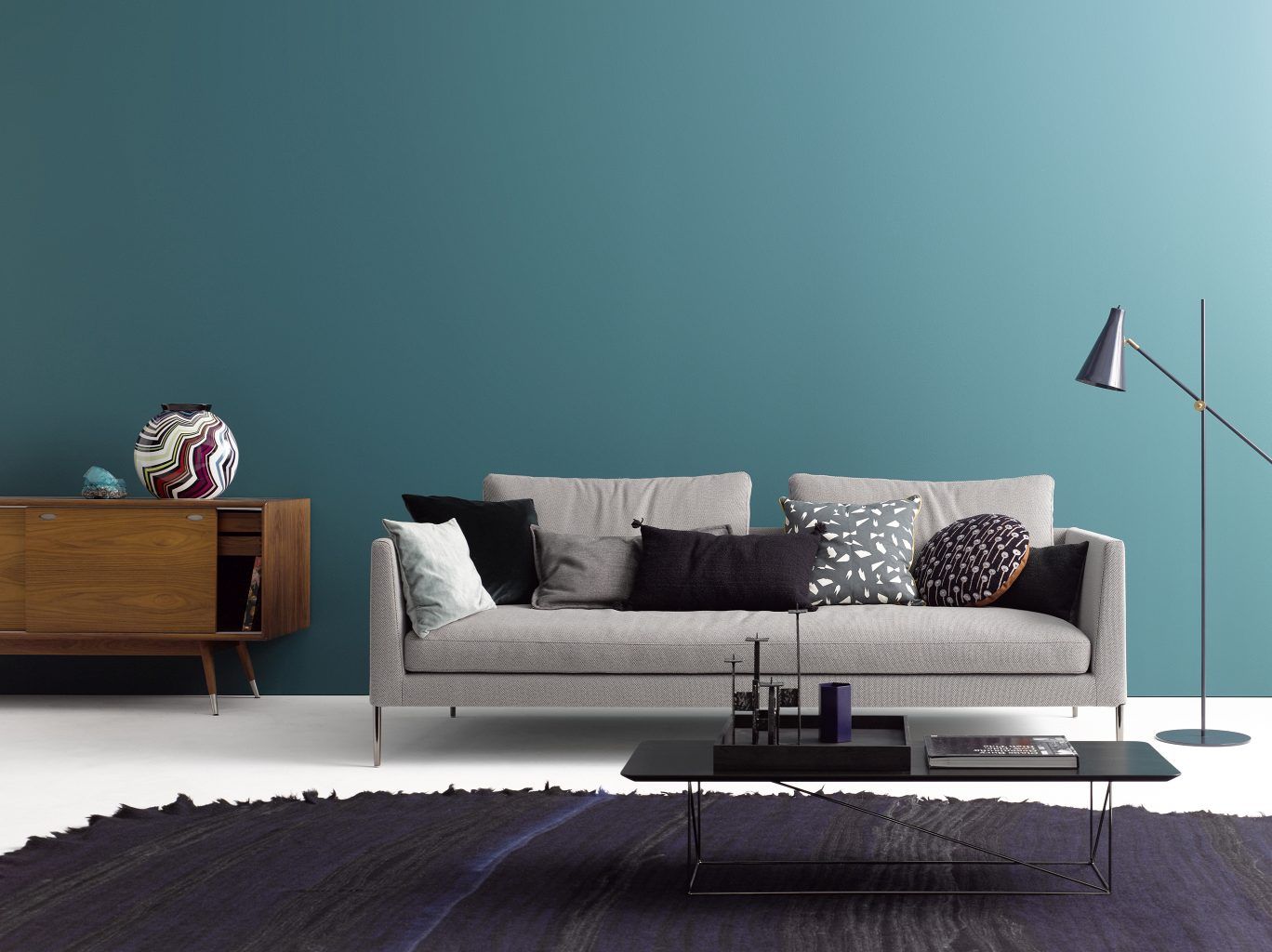 Graues Cor Sofa Pilotis ohne Rückenkissen mit Kissen, Teppich und Beistelltisch vor blauer Wand.