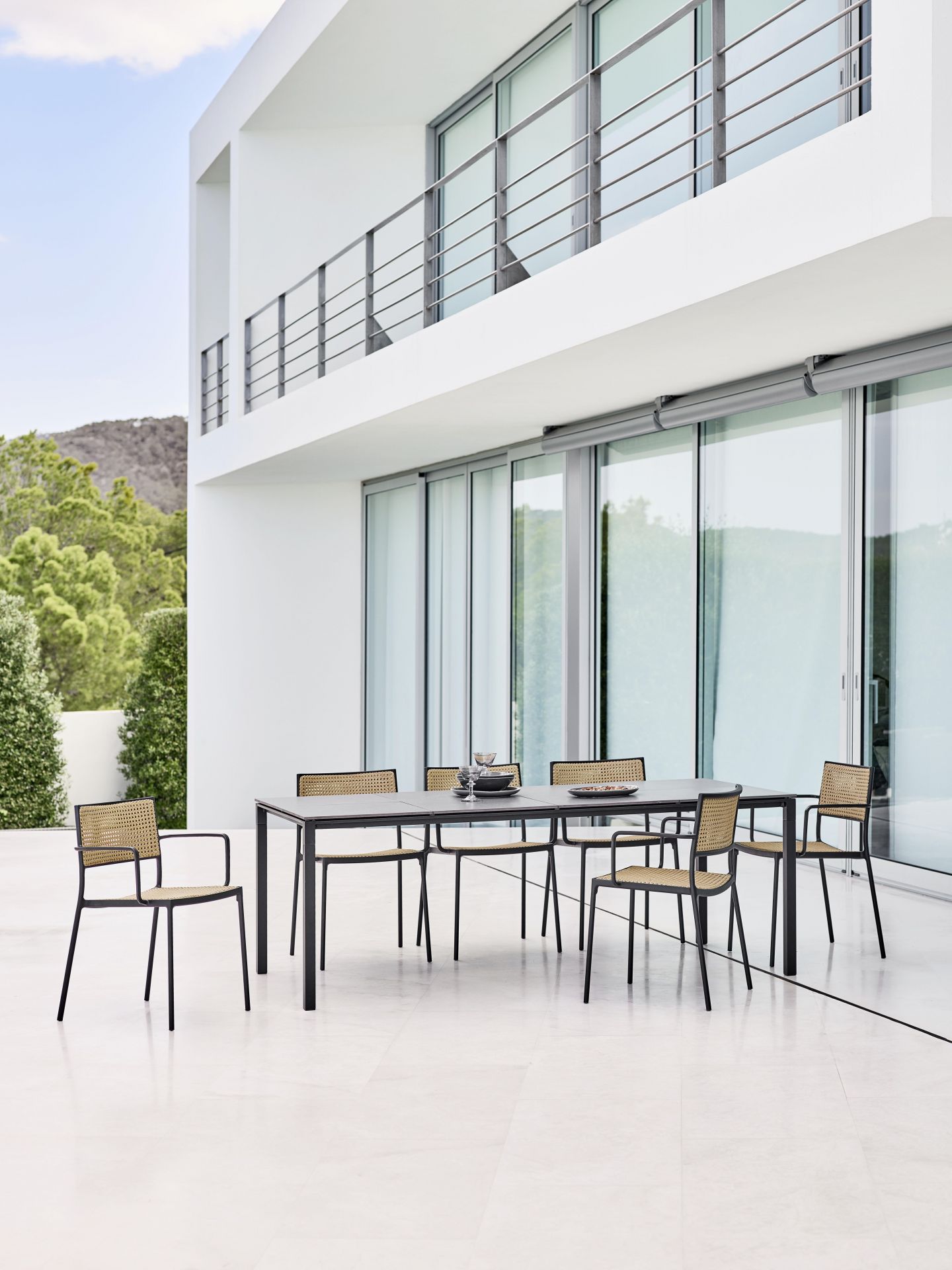 Cane-Line Pure Outdoor Esstisch mit Stühlen auf einer Terrasse vor einem modernen Haus.