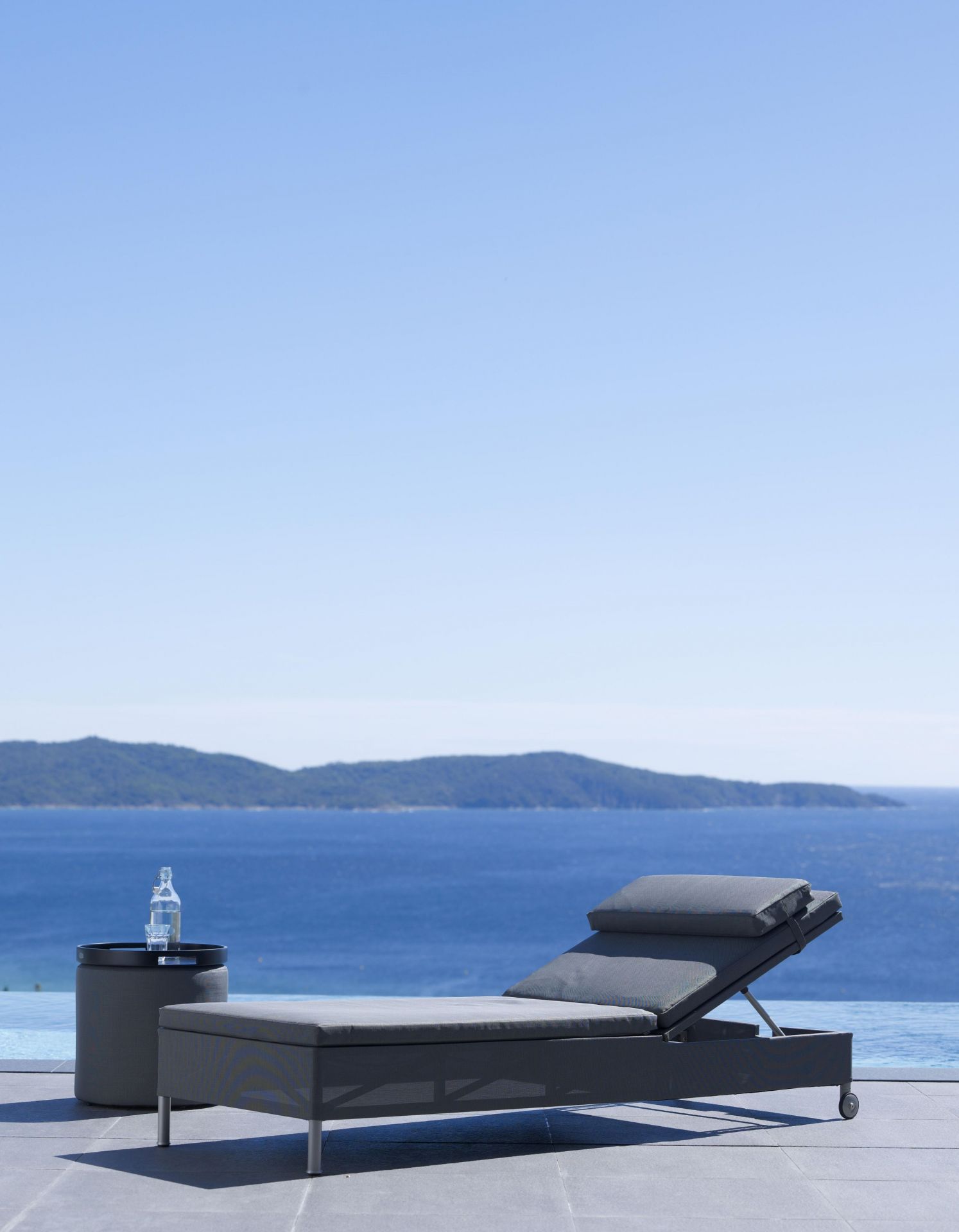 Cane-Line Rest Sonnenliege in Grau mit Beistelltisch und Meerblick für entspannte Stunden.