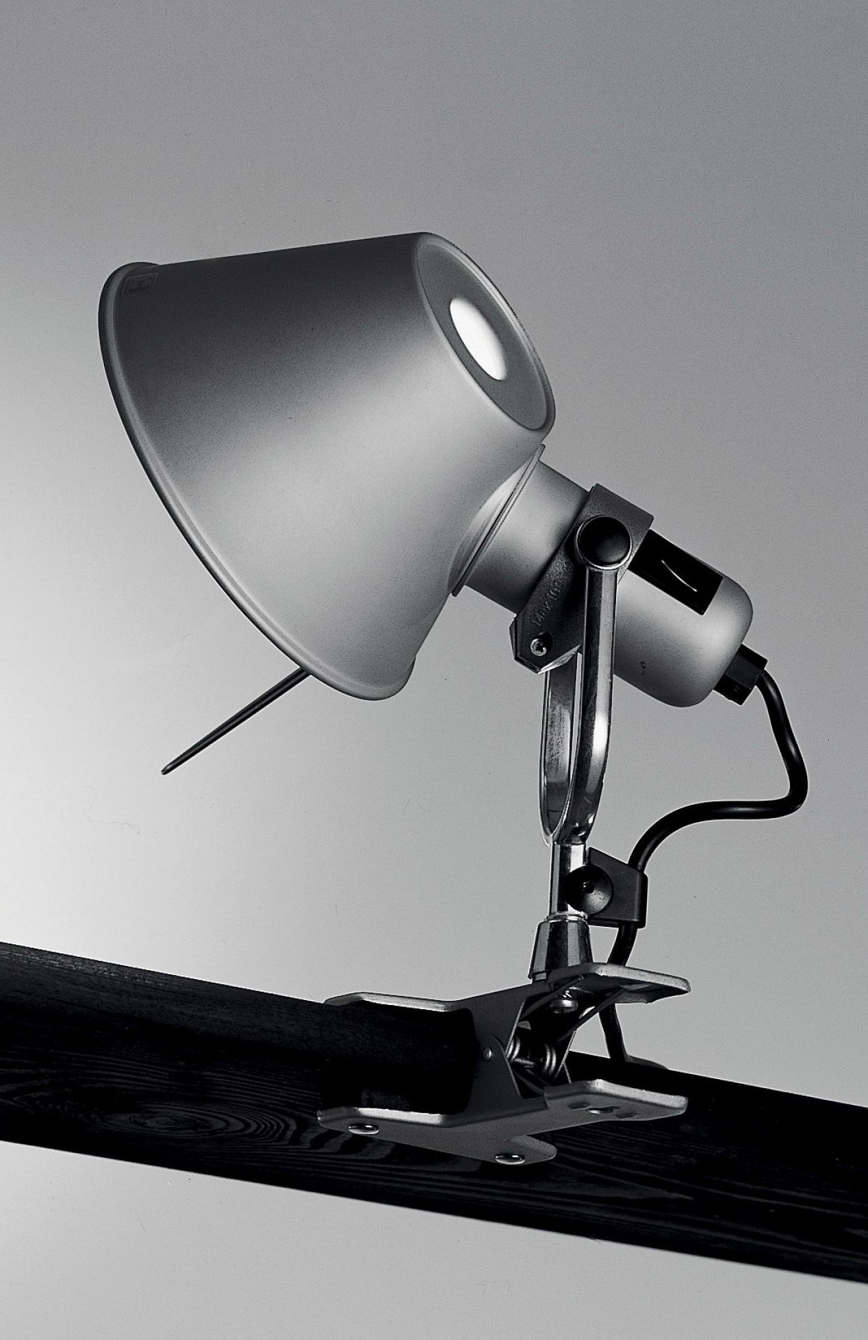 Nahaufnahme der Artemide Tolomeo Pinza Klemmleuchte aus Aluminium, befestigt an einem dunklen Holzbrett.