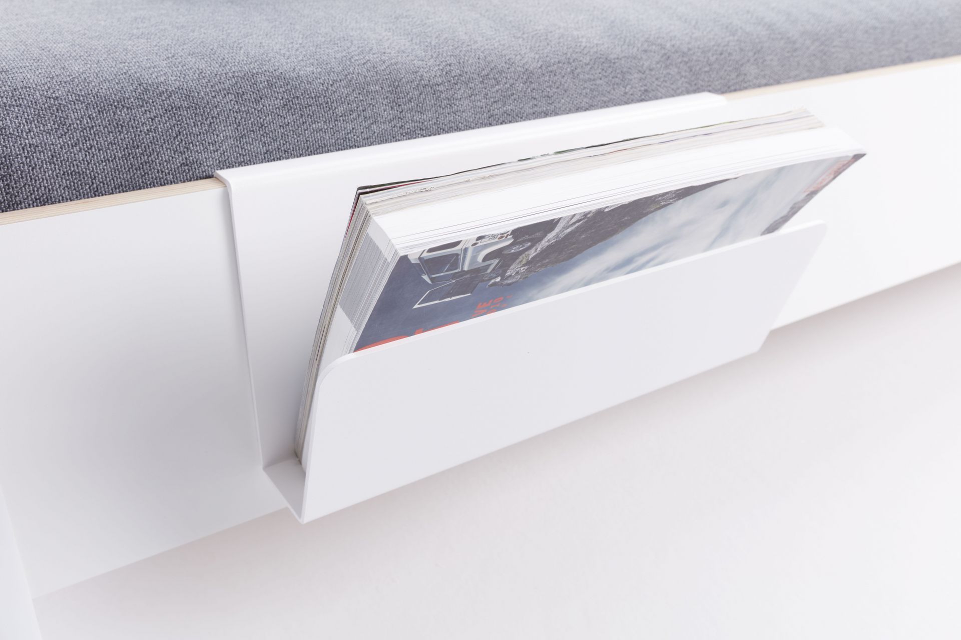 Weiße Zeitschriftenablage für Flai Bett von Müller Möbelwerkstätten, befestigt an einem Bett mit grauer Matratze.